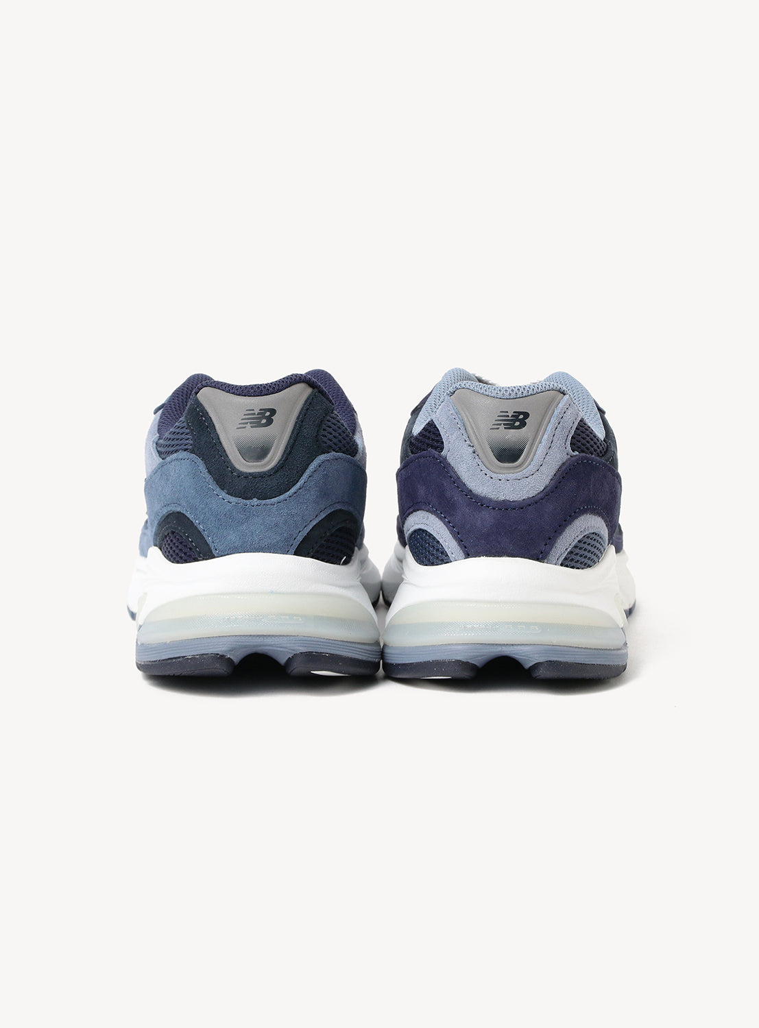 A pair of New Balance 2010 Exclusive Sneakers by BEAMS is shown from the back, showcasing an array of blue suede and mesh panels, white midsoles, and dark rubber outsoles against a white background. Inspired by the classic New Balance 2010 silhouette, these NEW BALANCE shoes blend retro style with modern comfort.
