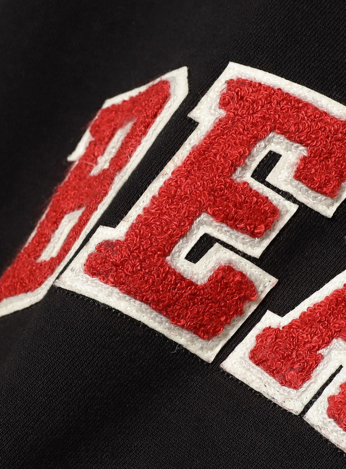 Close-up of red and white chenille letters sewn onto black fabric, showcasing the textured stitching detail on the BEAMS Basic Hoodie by BEAMS—designed for comfort and perfect for everyday wear.