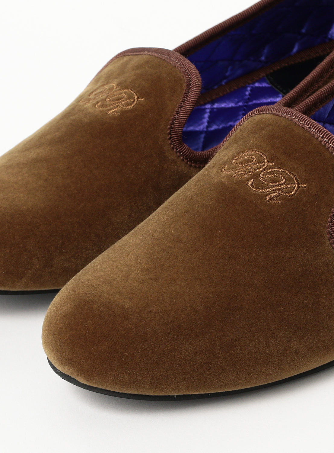 Close up of a pair of brown velvet shoes with quilted purple insole. 