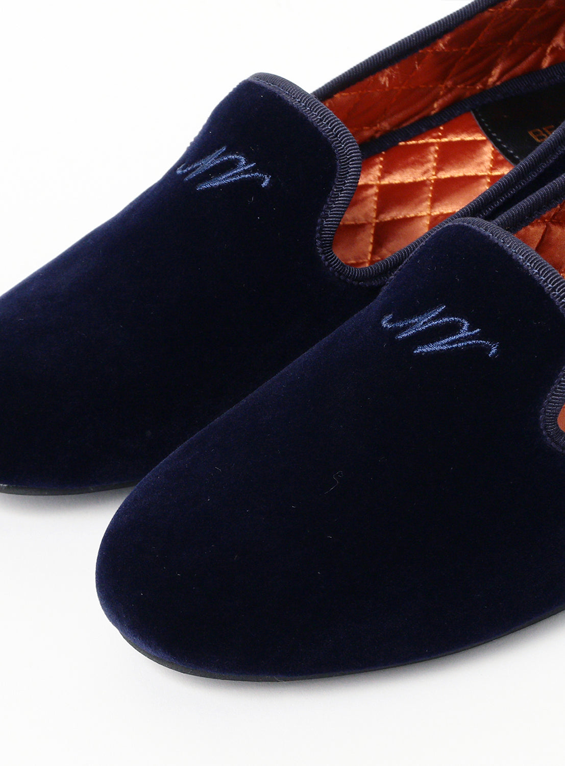 Pair of navy velvet slippers with quilted orange interior on a white background.