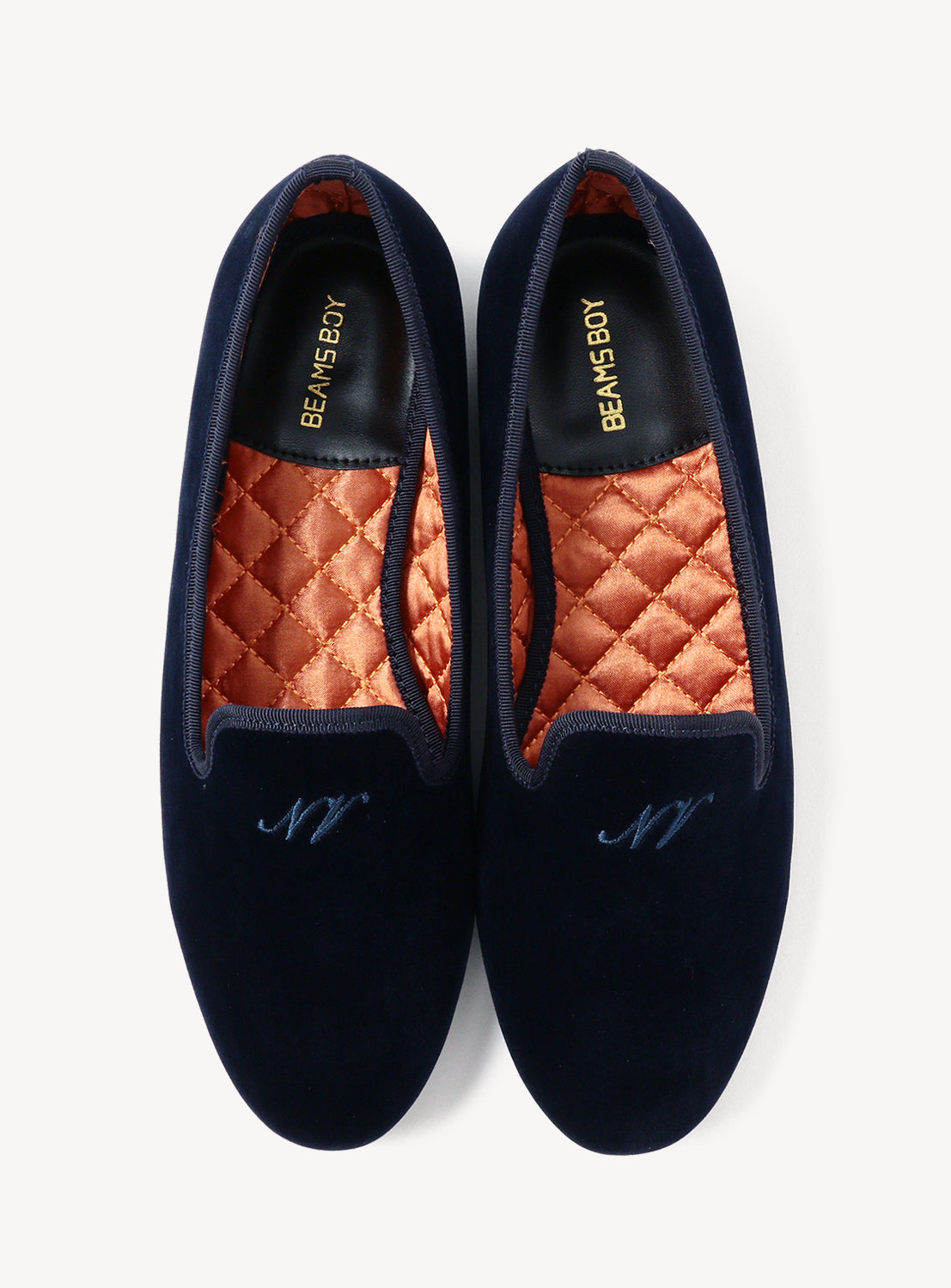 Pair of navy velvet slippers with quilted orange interior on a white background.