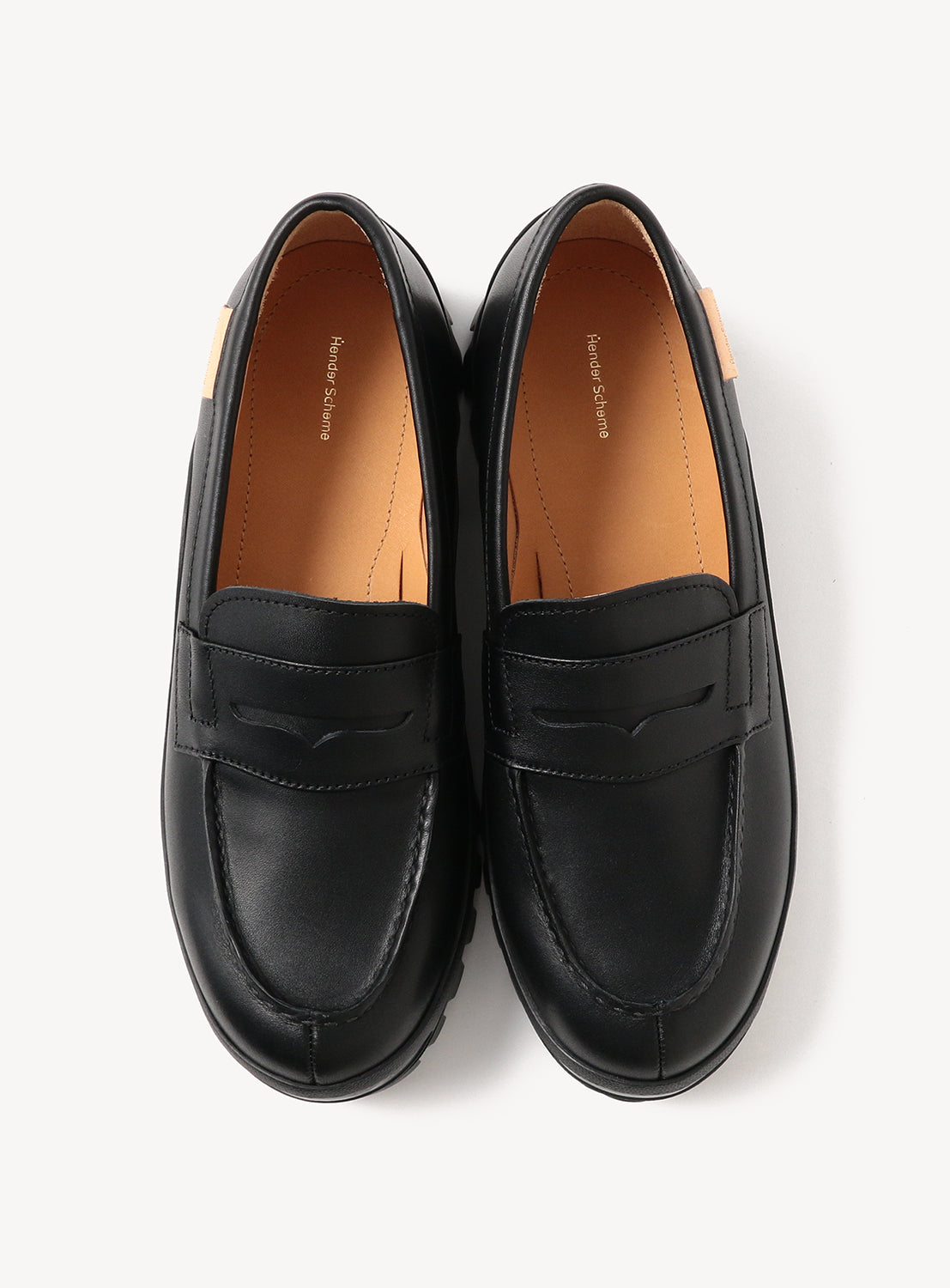 A pair of Hender Scheme Loafer #2146 shoes by Hender Scheme, featuring modern black leather uppers, tan insoles, and a durable Vibram outsole, viewed from above on a white background.