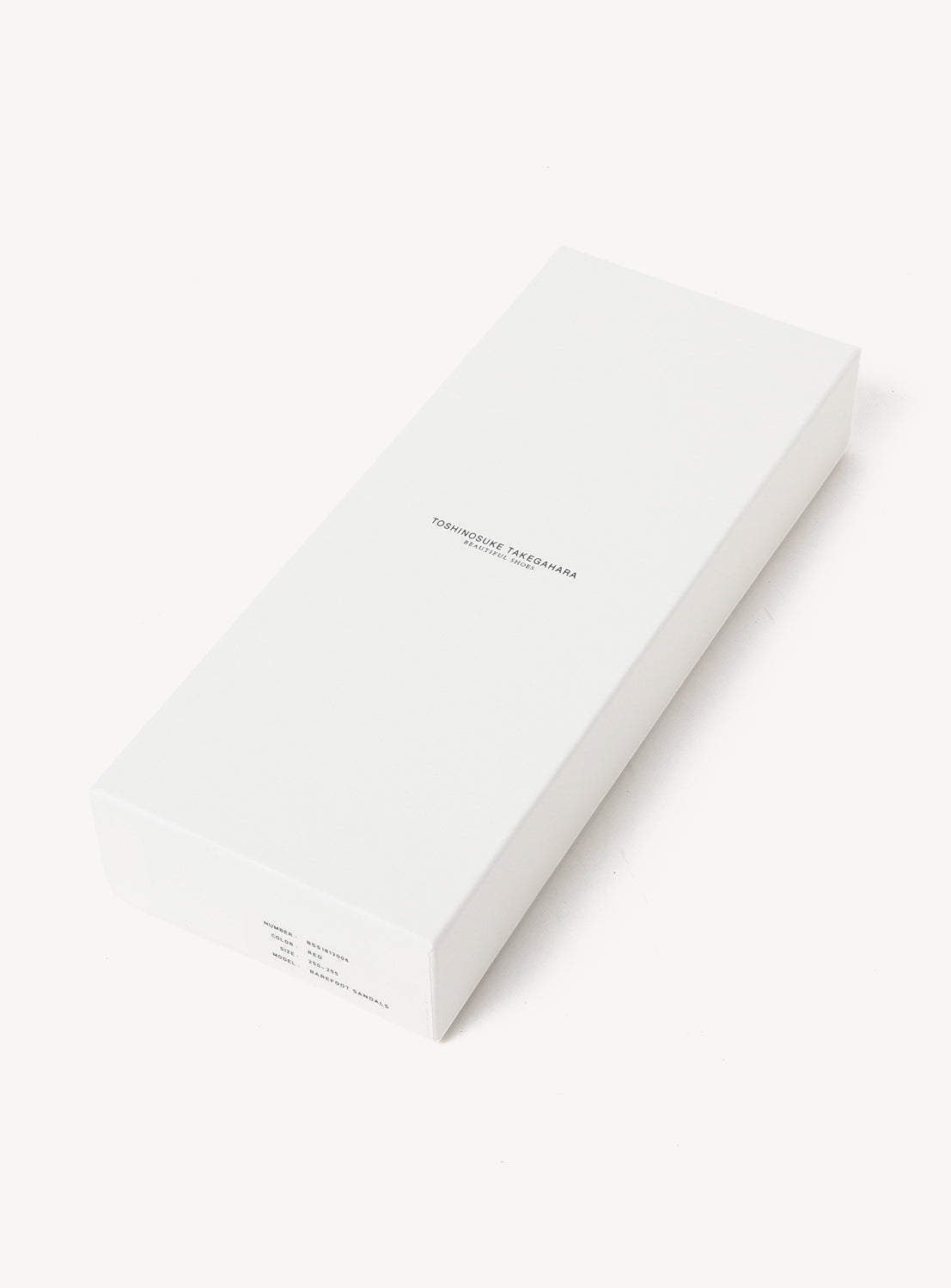 A rectangular white box from BEAUTIFUL SHOES, featuring understated black text on the top, is photographed against a white background. The box's simple, clean design and modern edges mirror the sleek aesthetic of the Minimalist Huarache Barefoot Sandals inside.