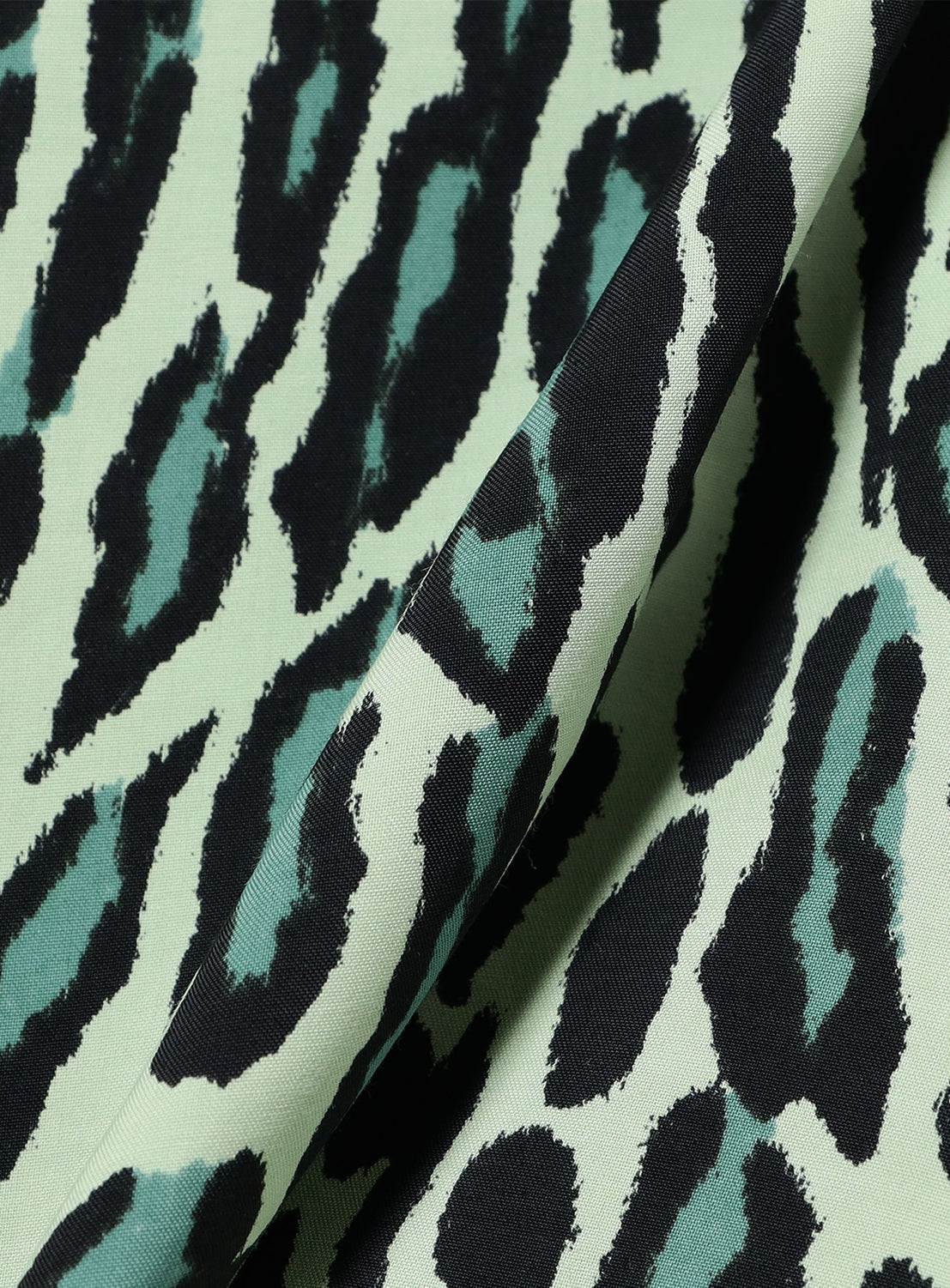 Close-up of fabric from the STAR OF HOLLYWOOD High-Density Rayon Open Shirt "OCELOT," featuring a green and black leopard print pattern reminiscent of vintage 1950s designs. The slightly folded fabric highlights its texture and irregular spots across the surface, evoking the classic style that made STAR OF HOLLYWOOD famous.