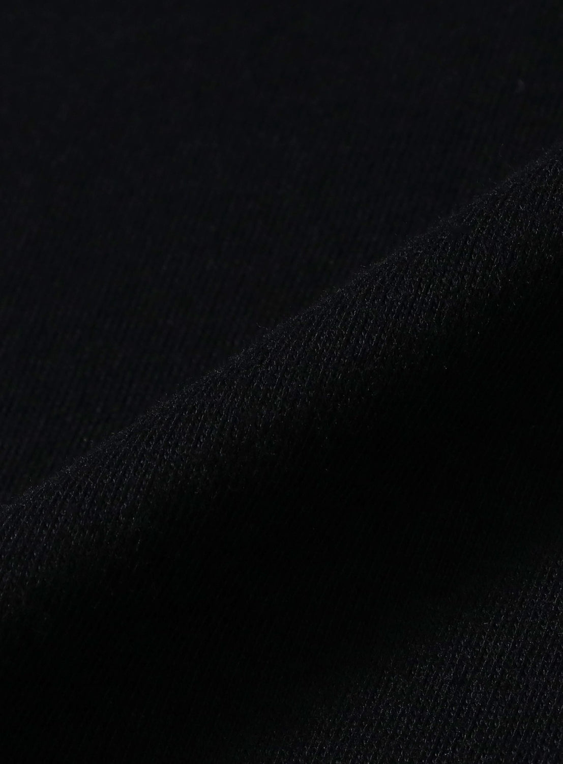 Close-up of a deep black fabric with a diagonal fold, revealing fine texture and subtle shadows—an ideal showcase for the understated style and distinct logo graphic featured on the Chaos Fishing Club 2026 Short Sleeve Logo T-Shirt.