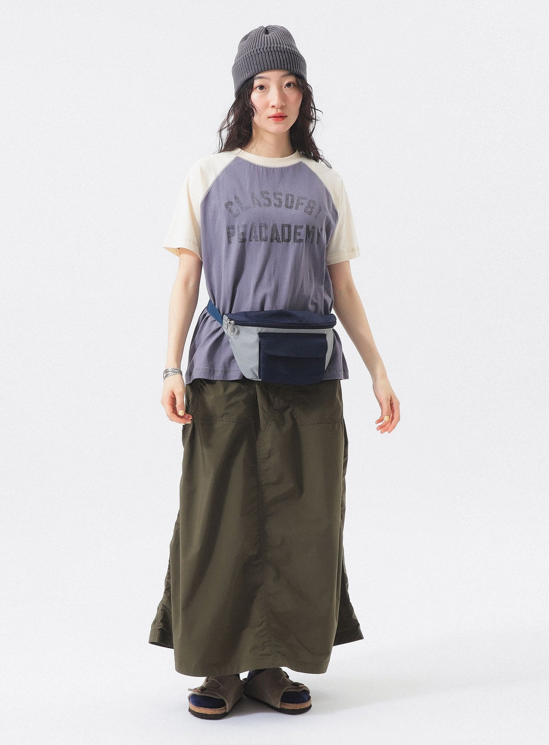 A woman in a gray beanie, BEAMS BOY Two-Tone Vintage Raglan T-shirt, long olive skirt, gray and blue waist bag, watch, and sandals stands against a white background for a relaxed vibe.