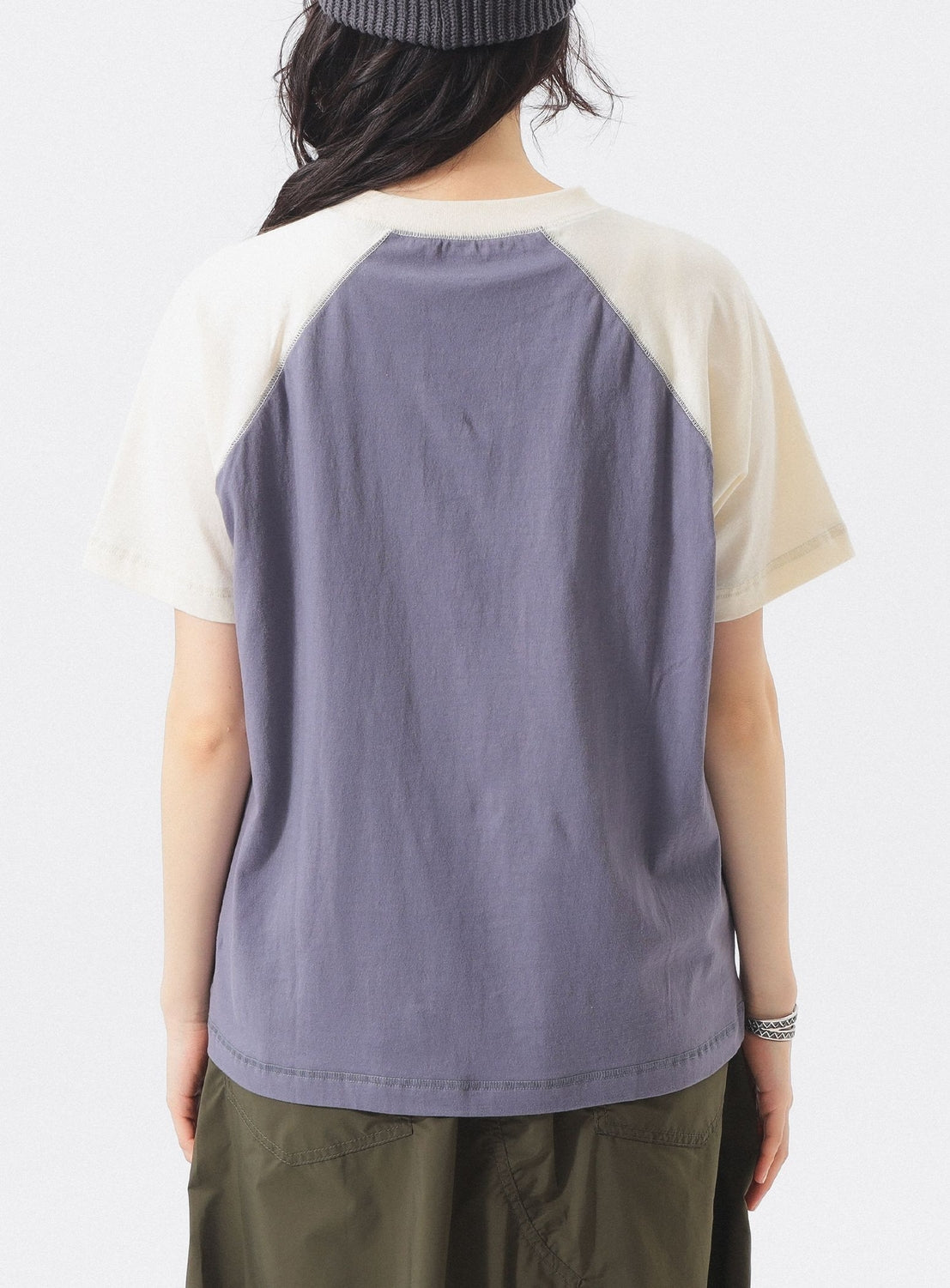 A person is seen from behind wearing a BEAMS BOY Two-Tone Vintage Raglan T-shirt with off-white sleeves and a purple body, styled with olive green pants and a dark knit beanie against a plain, light-colored background.