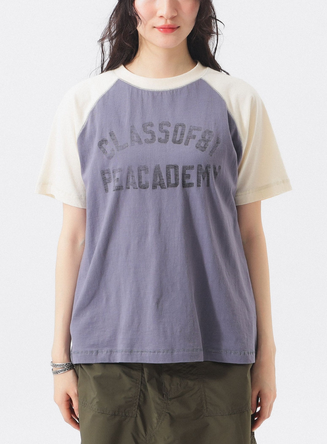Wearing the BEAMS BOY Two-Tone Vintage Raglan T-shirt with faded CLASS OF 91 PEACADEMY text and olive green pants, this look channels collegiate athletic style against a simple backdrop.