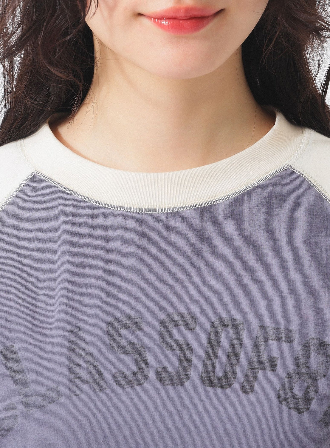 A close-up of a person with wavy dark hair wearing the BEAMS BOY Two-Tone Vintage Raglan T-shirt in faded lavender, featuring a white collar and partial "CLASS OF 8" text; only their lower face is visible, giving a worn-in vibe.