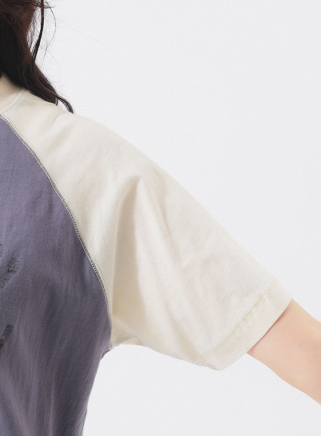 A close-up of a person wearing the BEAMS BOY Two-Tone Vintage Raglan T-shirt, featuring cream and dark gray color-blocked short sleeves with collegiate athletic vibes, shown from shoulder to elbow against a plain white background.