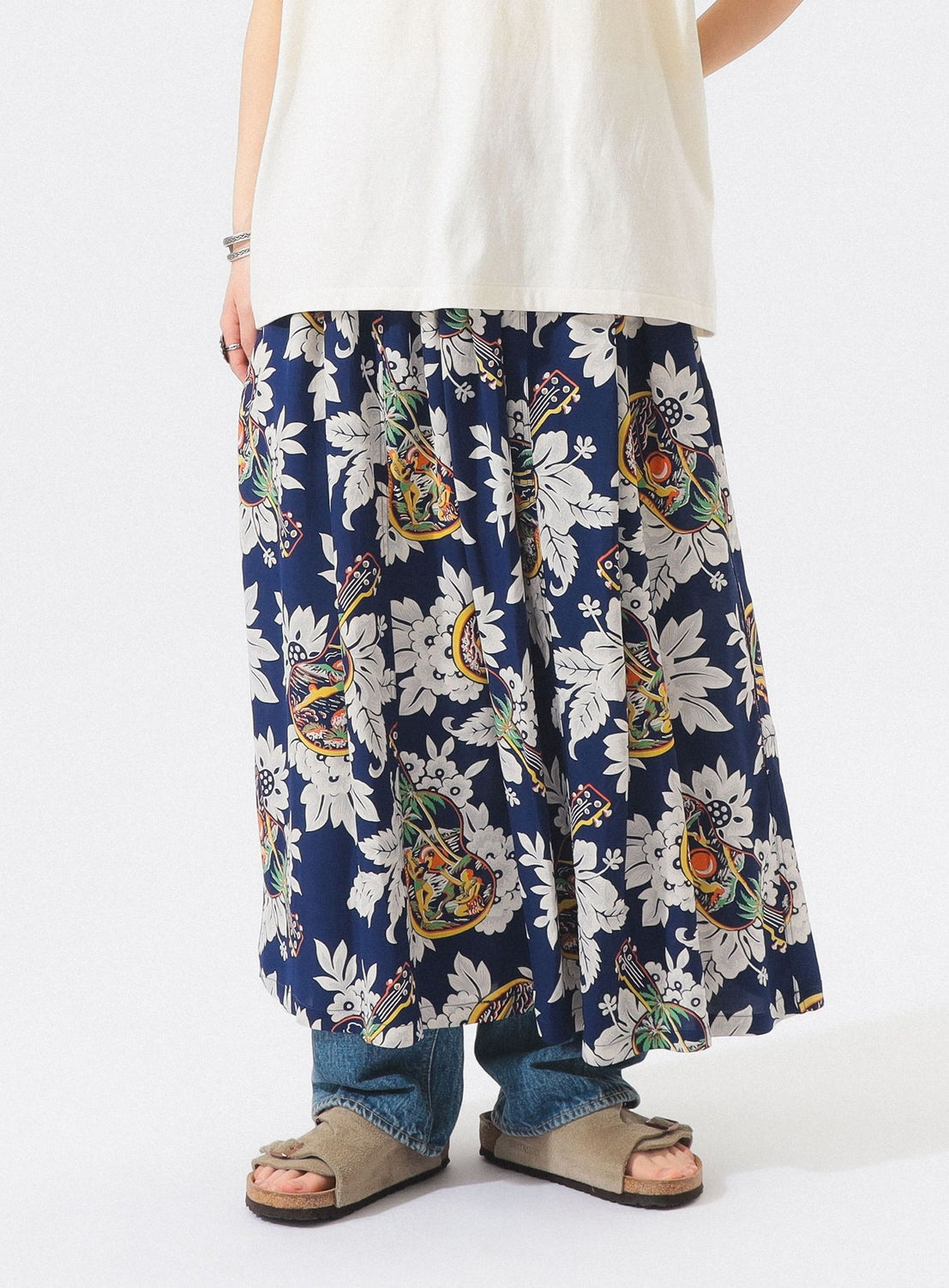 Person wearing blue jeans and beige sandals layered with the [Exclusive] SUN SURF x BEAMS BOY Aloha Gathered Long Skirt by SUN SURF. The image is cropped to show only the lower half of the body.