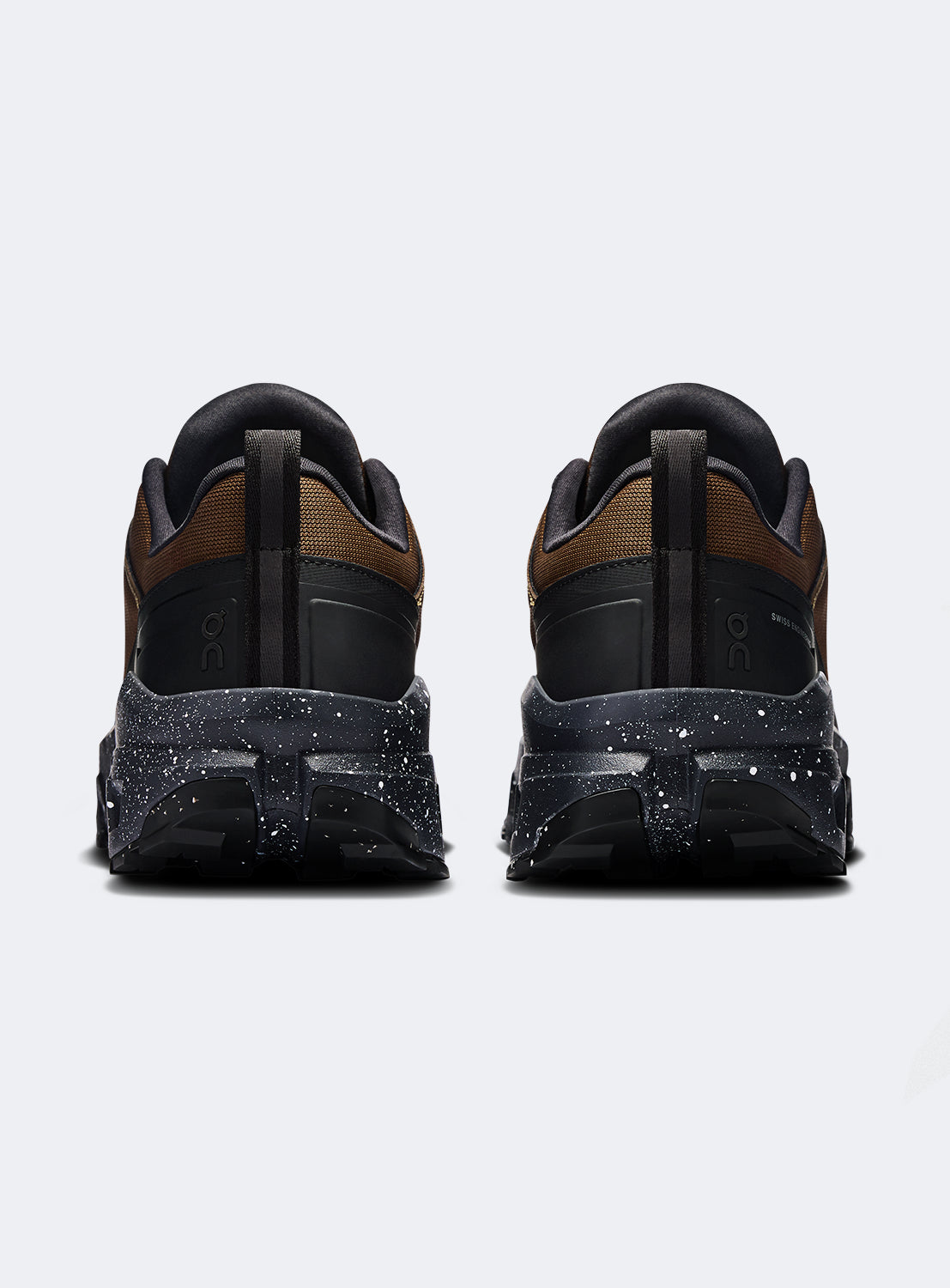 Back of a pair of brown and black hiking shoes with a black speckled sole. 