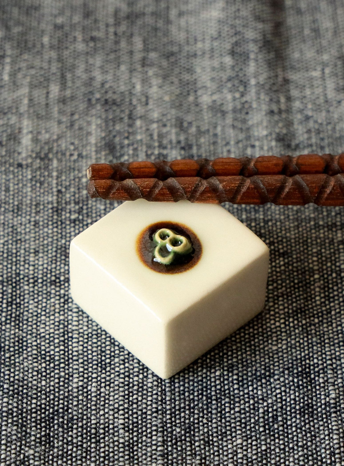 White hexagonal chopstick rest with a small black and brown design on a textured gray surface