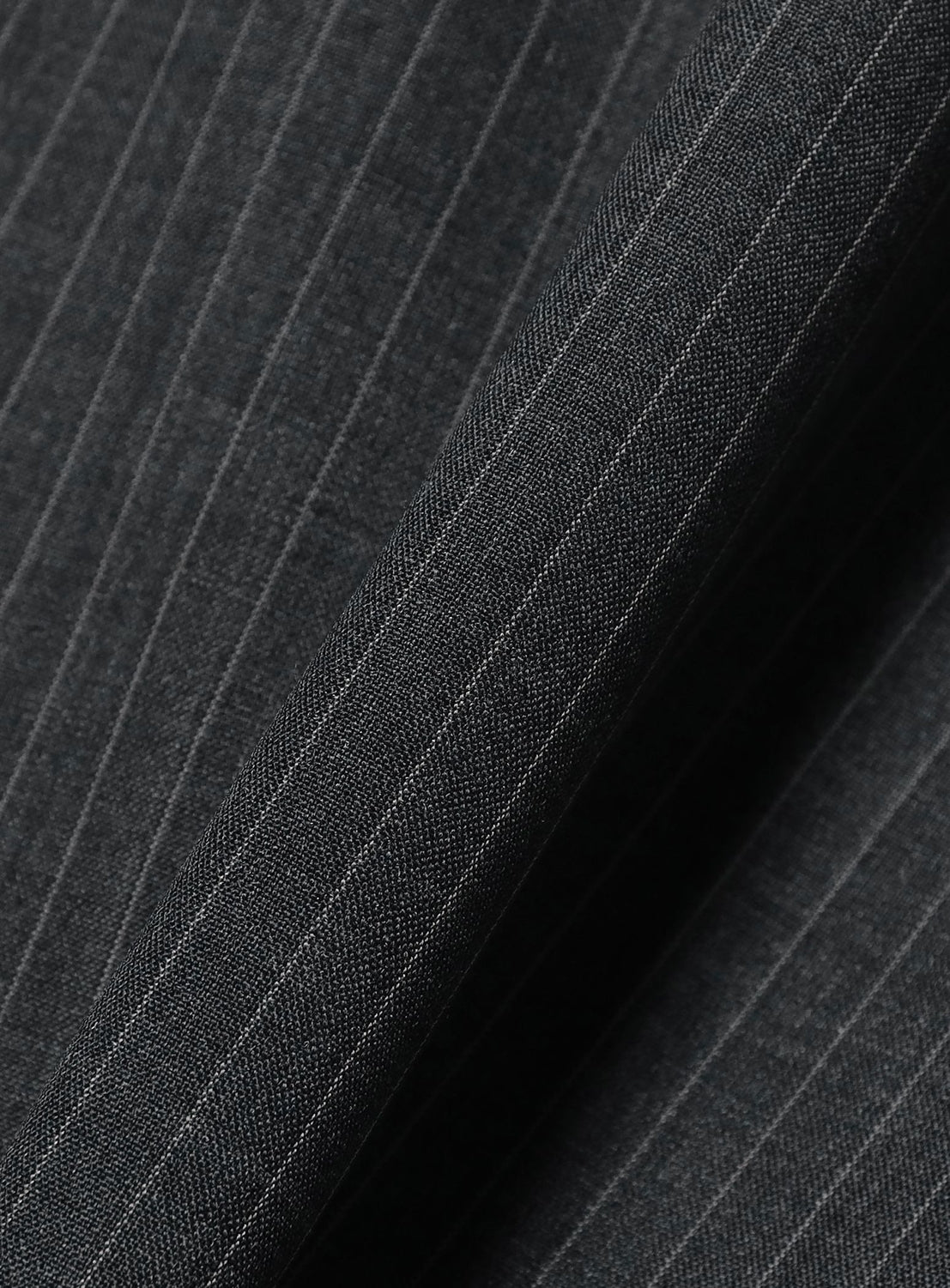 Close-up of a dark gray polyester-wool tropical fabric with fine, evenly spaced light vertical lines—as featured in the BEAMS TW Wide Fit Half-Zip Shirt. The slightly folded textile reveals its texture and subtle sheen, making it ideal for crafting a relaxed silhouette or an elegant pullover like this signature BEAMS piece.