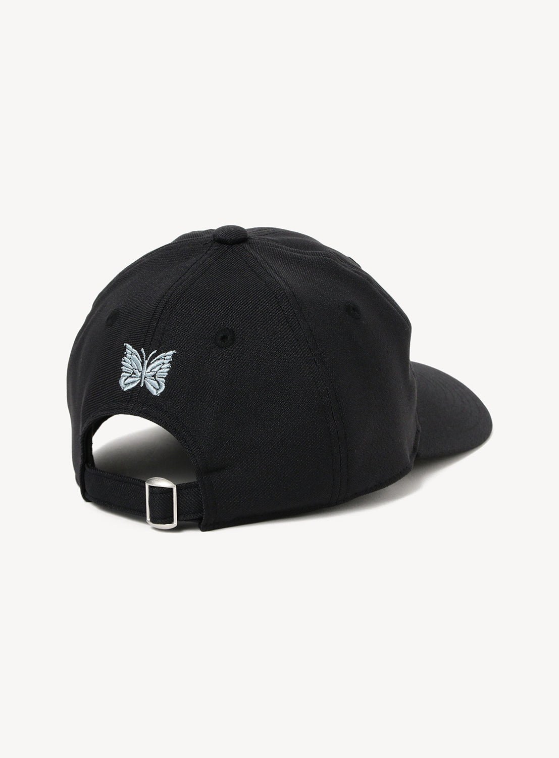 An [Exclusive] Needles 50th Baseball Cap by NEEDLES in black is shown from the back. Above the adjustable strap with a silver metal buckle, there is a small, light blue custom embroidered butterfly logo. The background is plain white.