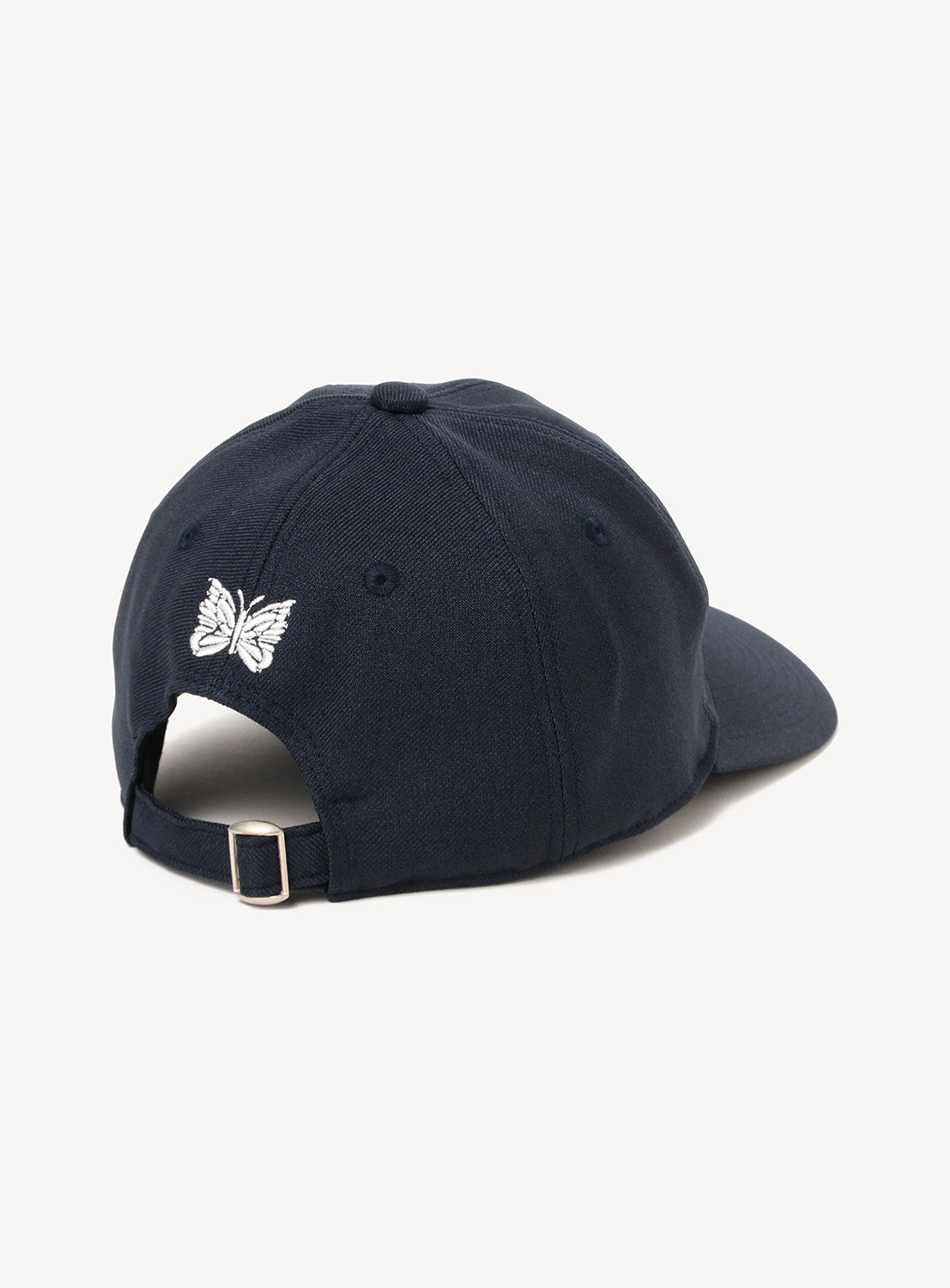 An exclusive Needles 50th Baseball Cap by NEEDLES, showcased from the back in deep navy, features custom white butterfly embroidery above an adjustable strap with a silver metal buckle—part of a special collaboration release.