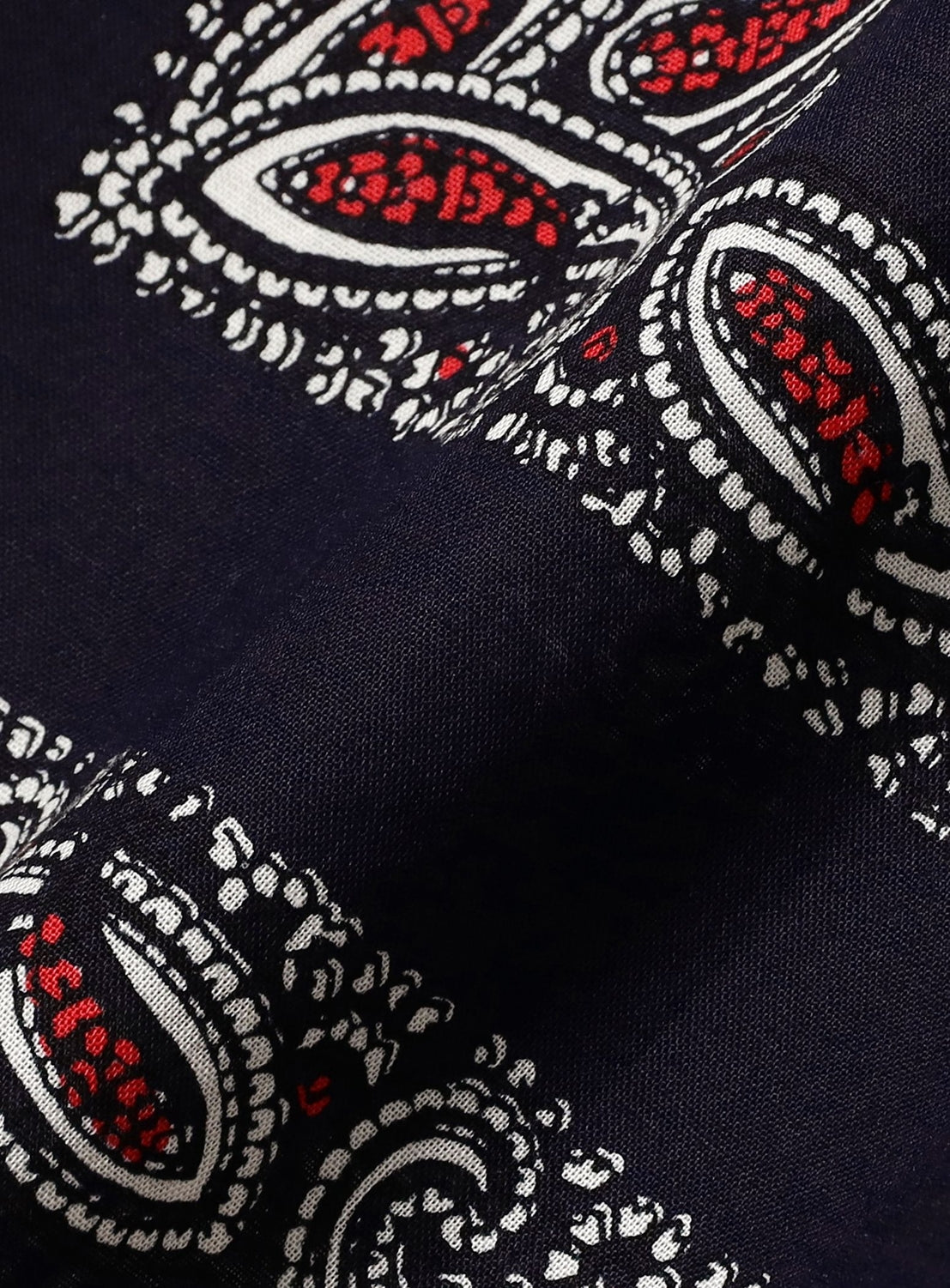 Detailed view of the Paisley Open Collar Shirt by NOMARHYTHM TEXTILE, featuring dark fabric adorned with a white and red paisley print. The pattern showcases teardrop motifs and dotted outlines on gently crinkled fabric—ideal for standing out in style.