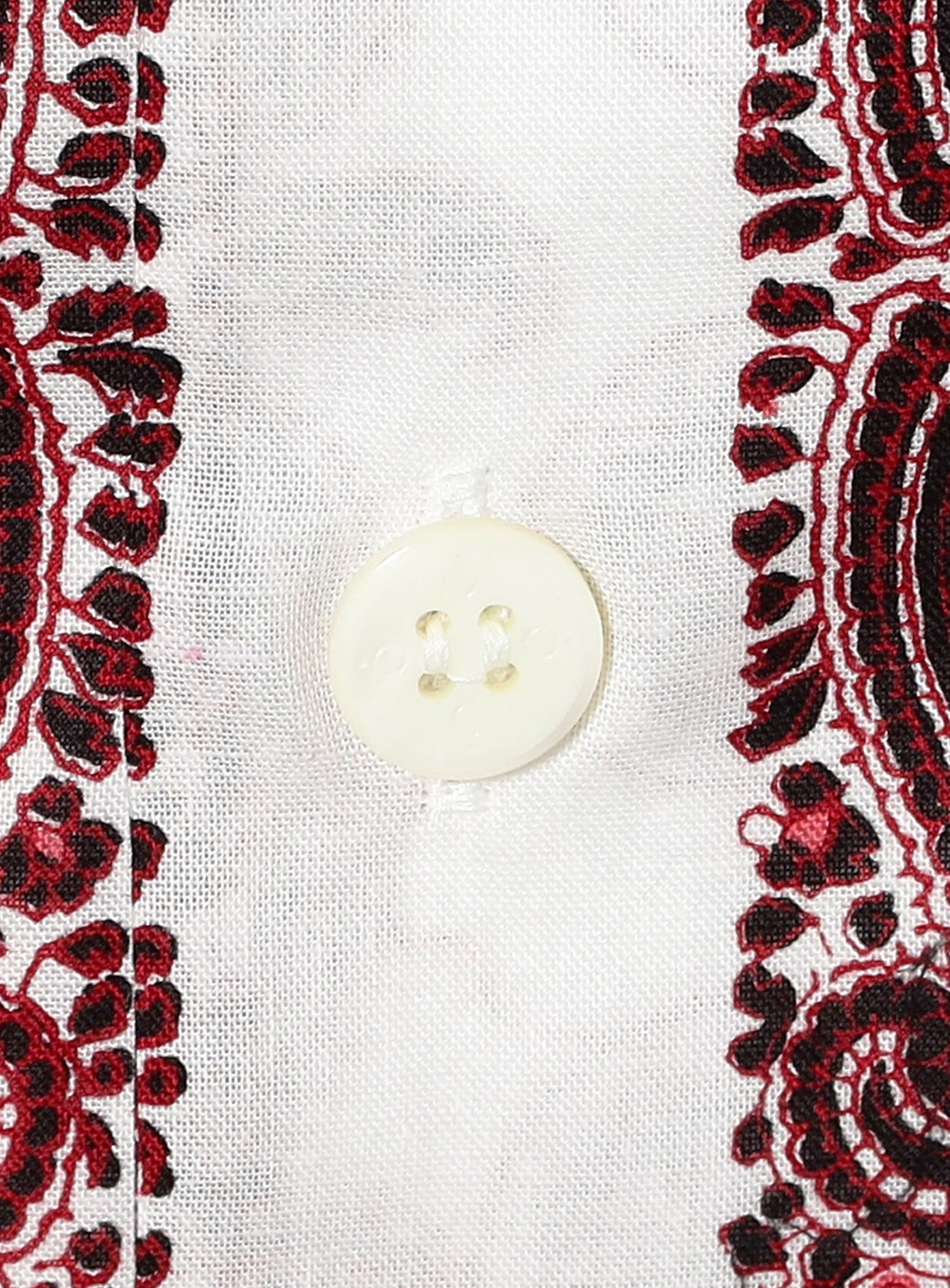 A close-up of a white button on white fabric, bordered by intricate red and black paisley print patterns on each side, showcases the stylish Paisley Open Collar Shirt from NOMARHYTHM TEXTILE.