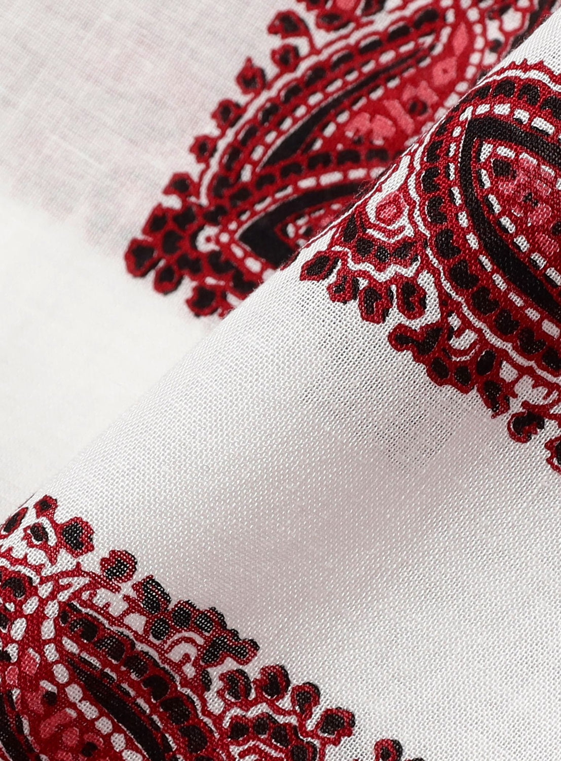 Close-up of the Paisley Open Collar Shirt by NOMARHYTHM TEXTILE, featuring an intricate red and black paisley print on white fabric. The detailed design and delicate weave are highlighted as the shirt is gently folded—perfect for crafting a stylish statement piece.
