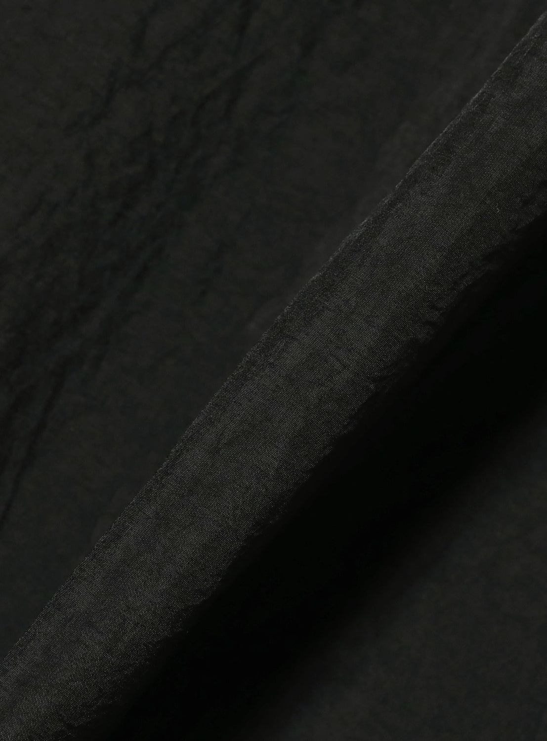A close-up of the TEATORA CAMBRIAN Short Sleeve Shirt - HOVER LAYER UNIT-01 by TEATORA shows black textured fabric, folded at an angle with visible creases and a matte finish—perfect for a lightweight performance shirt that balances comfort and style.