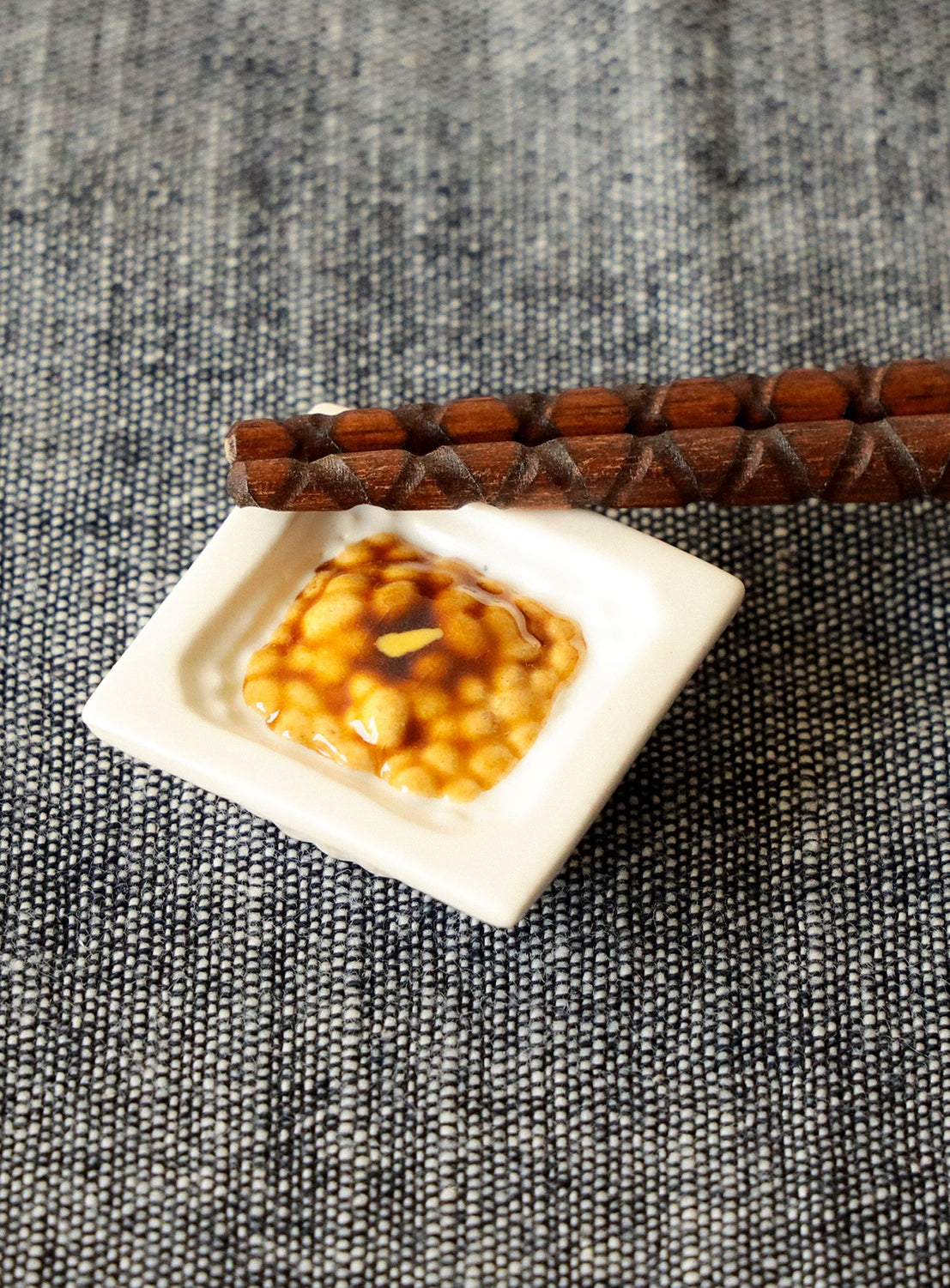 Small dish of food chopstick rest on a textured surface with wooden chopsticks