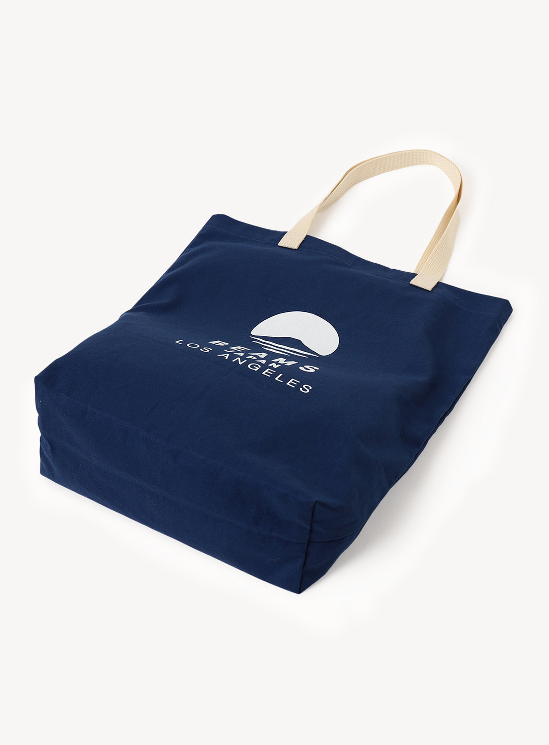 Introducing the [Exclusive] BEAMS JAPAN LA Tote Bag by BEAMS JAPAN—a navy blue Japanese cotton canvas tote with cream-colored handles. The front features a white semicircle graphic and “LOS ANGELES” text, inspired by the iconic BEAMS Japan Los Angeles tote. This durable, minimalist bag combines everyday versatility with stylish design.
