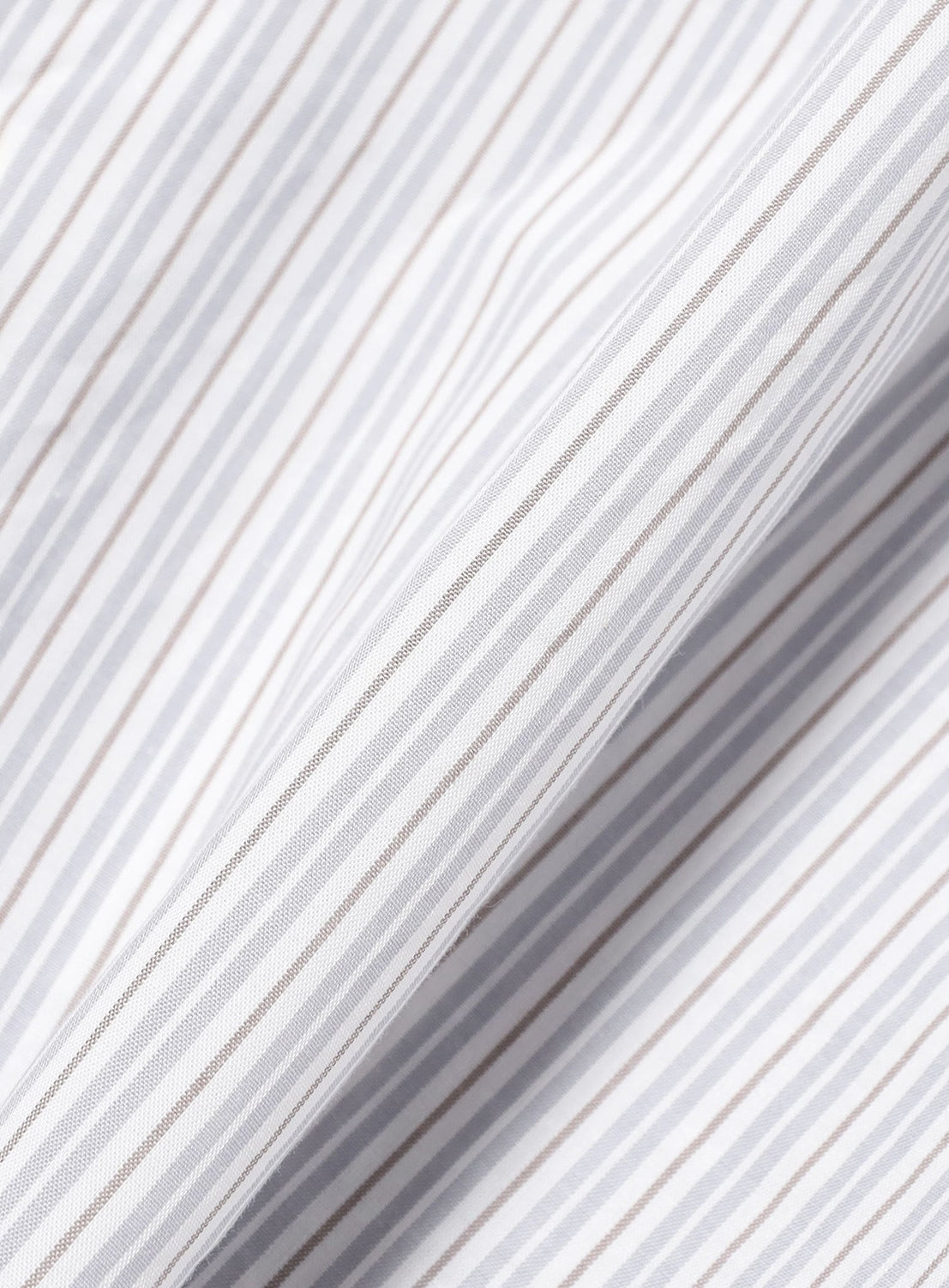 Close-up of the BEAMS Relaxed Fit Striped Shirt’s white fabric, showcasing thin, evenly spaced vertical gray and light brown stripes, with gentle folds that create soft shadows and a textured appearance.