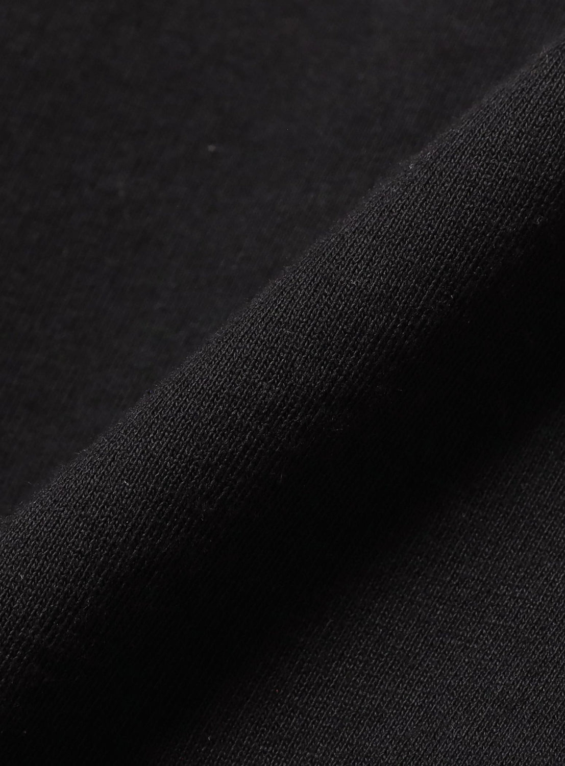 A close-up view of folded black fabric from the F-LAGSTUF-F x RYOTA DAIMON Long Sleeve Tee, highlighting its smooth texture and fine weave pattern under light—a detail that echoes the meticulous craftsmanship of RYOTA DAIMON's artwork.
