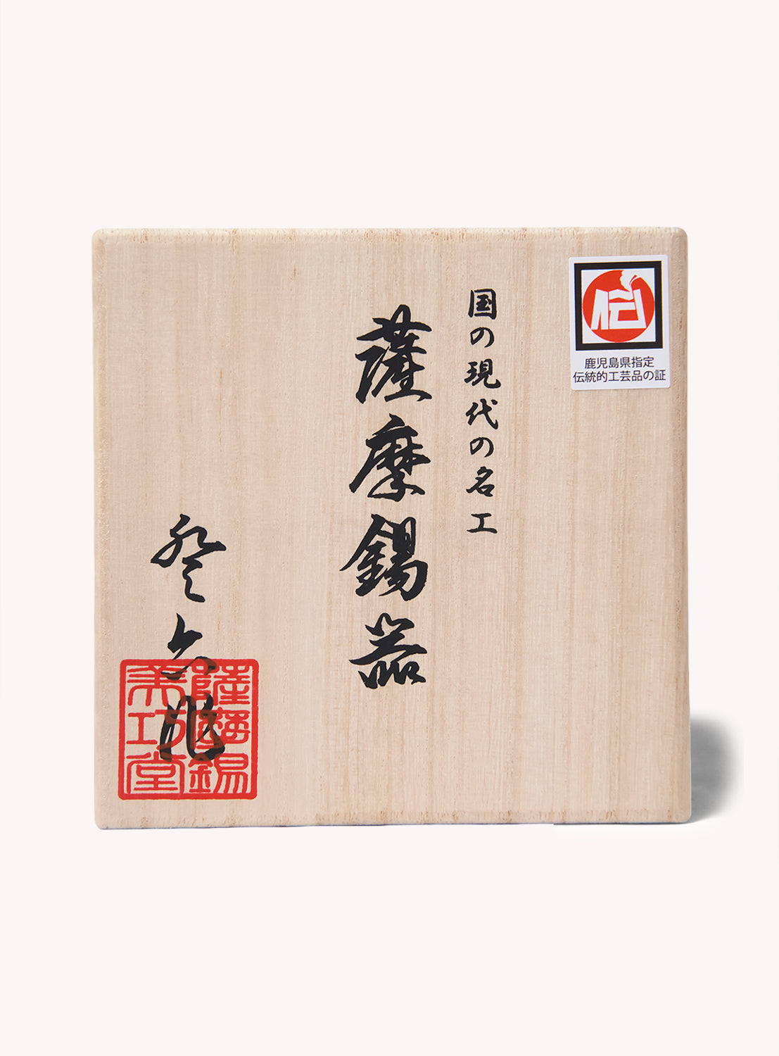 A square wooden box featuring Japanese calligraphy and red seals on the front, along with a small sticker in the top right corner, is photographed against a white background. This carefully crafted box hints at its premium contents—the SATSUMA x BEAMS JAPAN Smart Tumbler from BEAMS JAPAN.