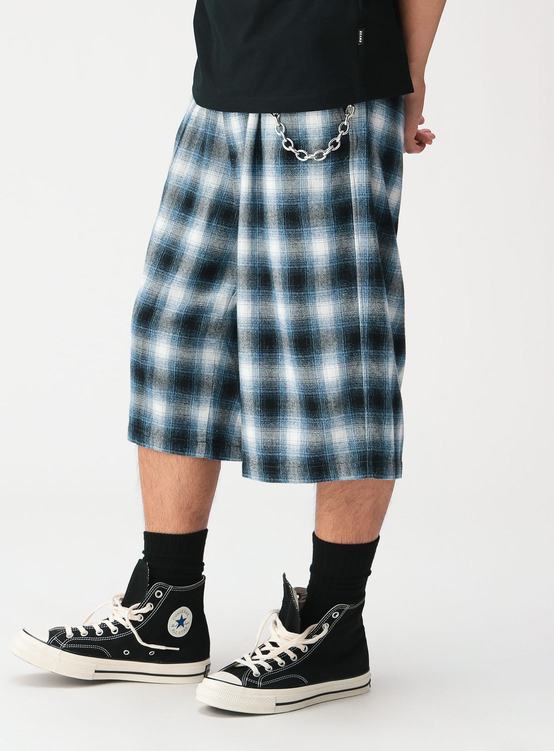 A person wearing BEAMS Check Shorts in a relaxed fit blue and white ombre check pattern with a silver chain attached to the waistband, paired with black high-top sneakers and black socks.