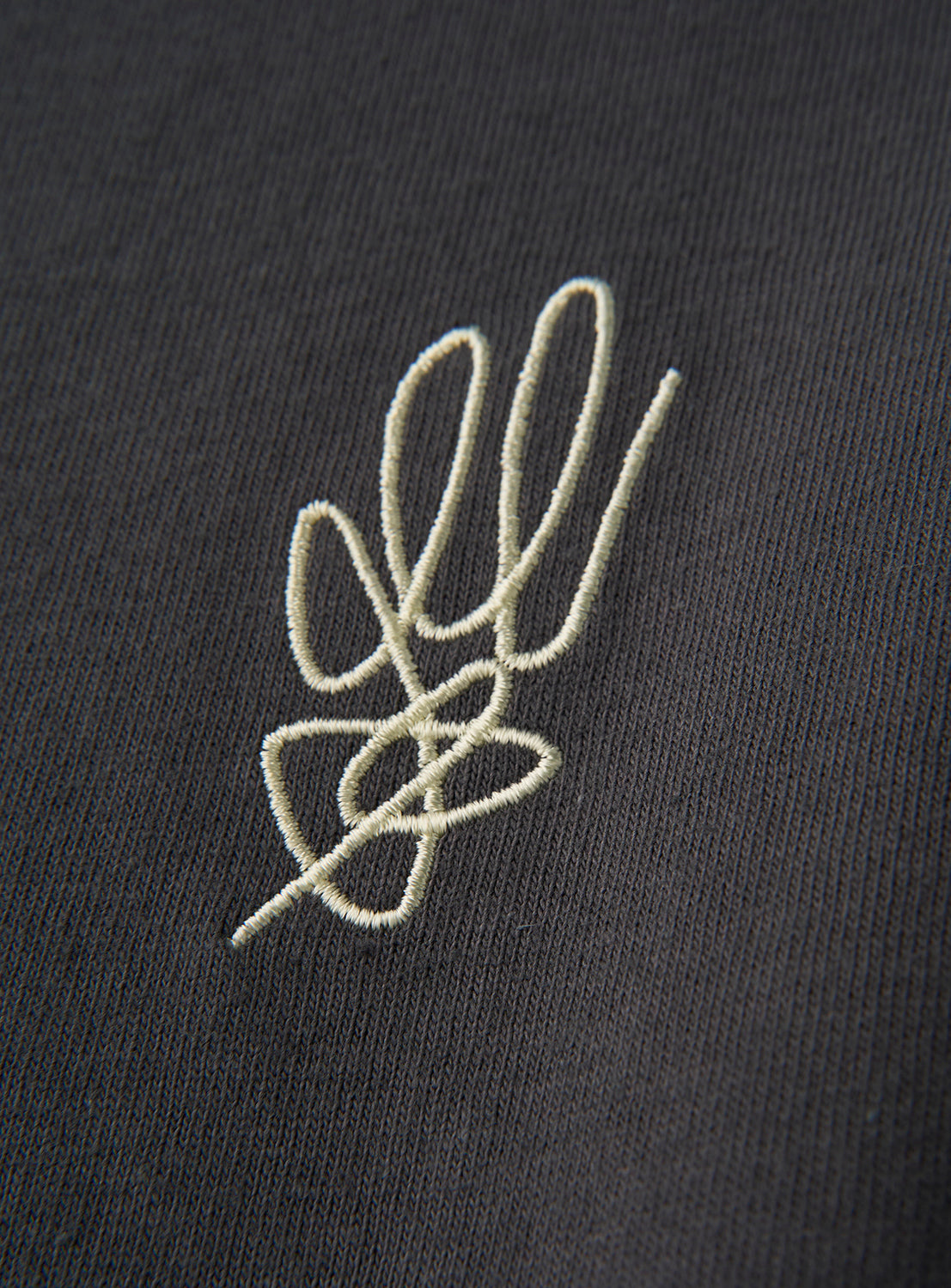 A close-up of the norahi Starskel Hologram T-Shirt by norahi, showcasing black fabric adorned with an abstract white embroidery design of overlapping, looping lines inspired by a hand-drawn motif.