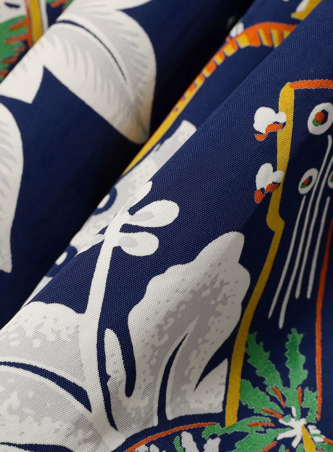 Close-up of the [Exclusive] SUN SURF x BEAMS BOY Aloha Gathered Long Skirt by SUN SURF, showcasing abstract white shapes, green leaves, and orange-yellow lines on a dark blue background—ideal for vintage Hawaiian-inspired style.