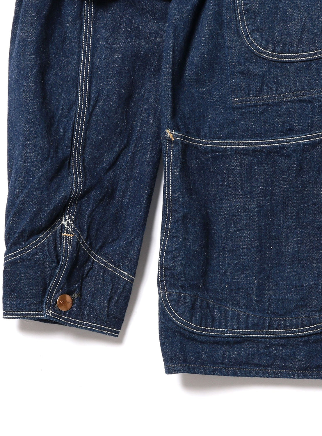 Close-up of the sleeve and pocket of orSlow’s 1950 Denim Coverall Jacket, showcasing its lightweight denim fabric with white contrast stitching and a brown button on the cuff. The textured, subtly speckled Japanese-made material highlights the quality craftsmanship of this classic piece.