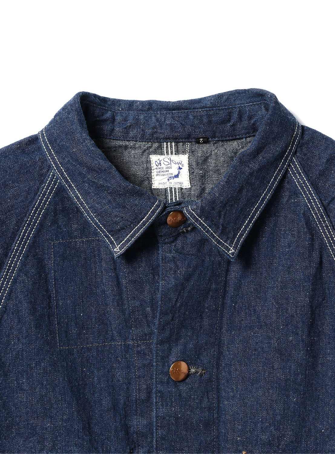 A close-up of the orSlow 1950 Denim Coverall Jacket, featuring blue lightweight denim fabric with white stitching, brown buttons, and a visible inside collar tag, made in Japan.