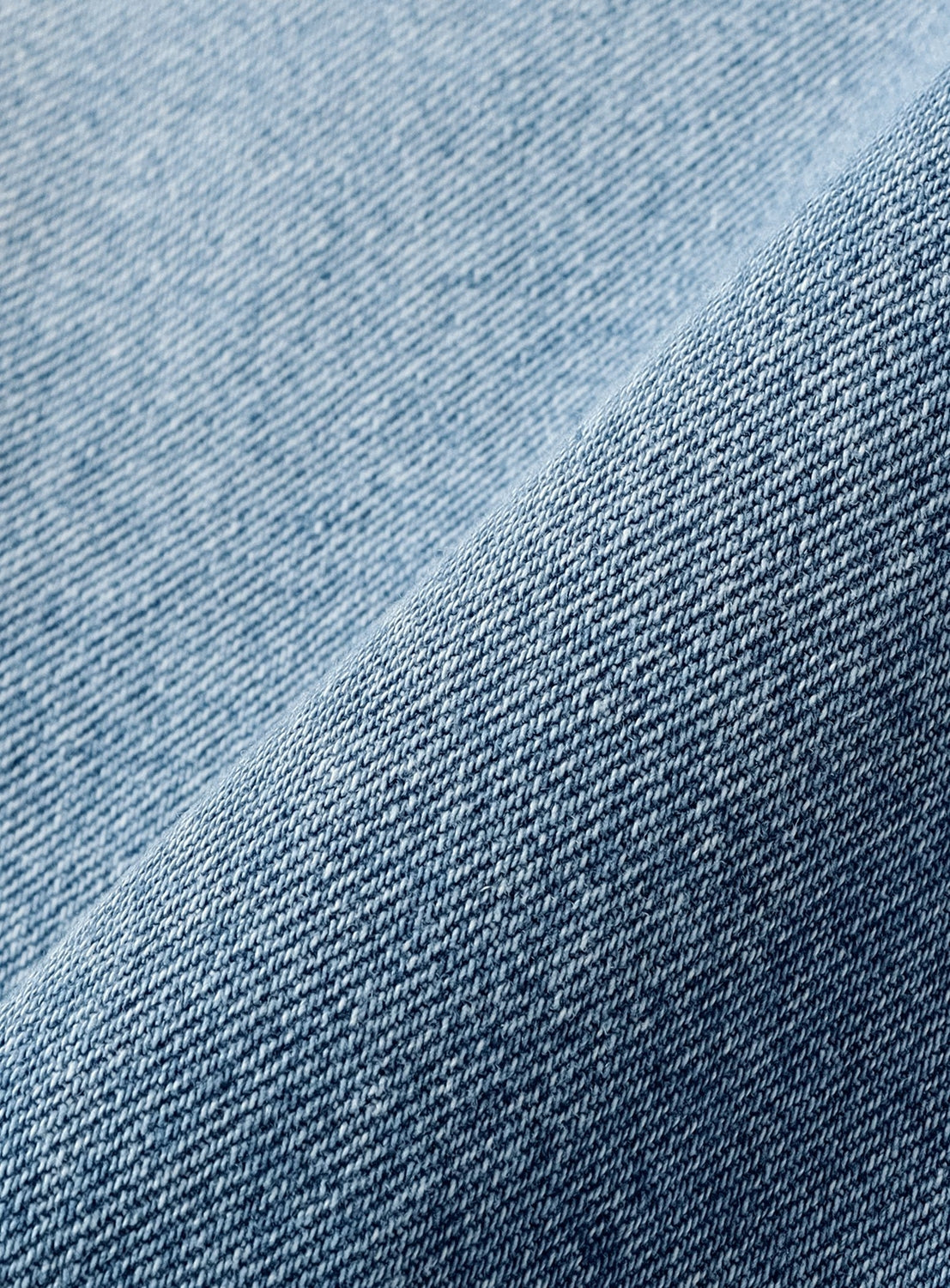 Close-up of light blue denim fabric with a visible weave pattern, showcasing texture and a gentle fold that emphasizes the textile’s thickness and durability—capturing the painter pant-inspired craftsmanship behind the BEAMS T Tyrrell Winston - Denim Shorts.
