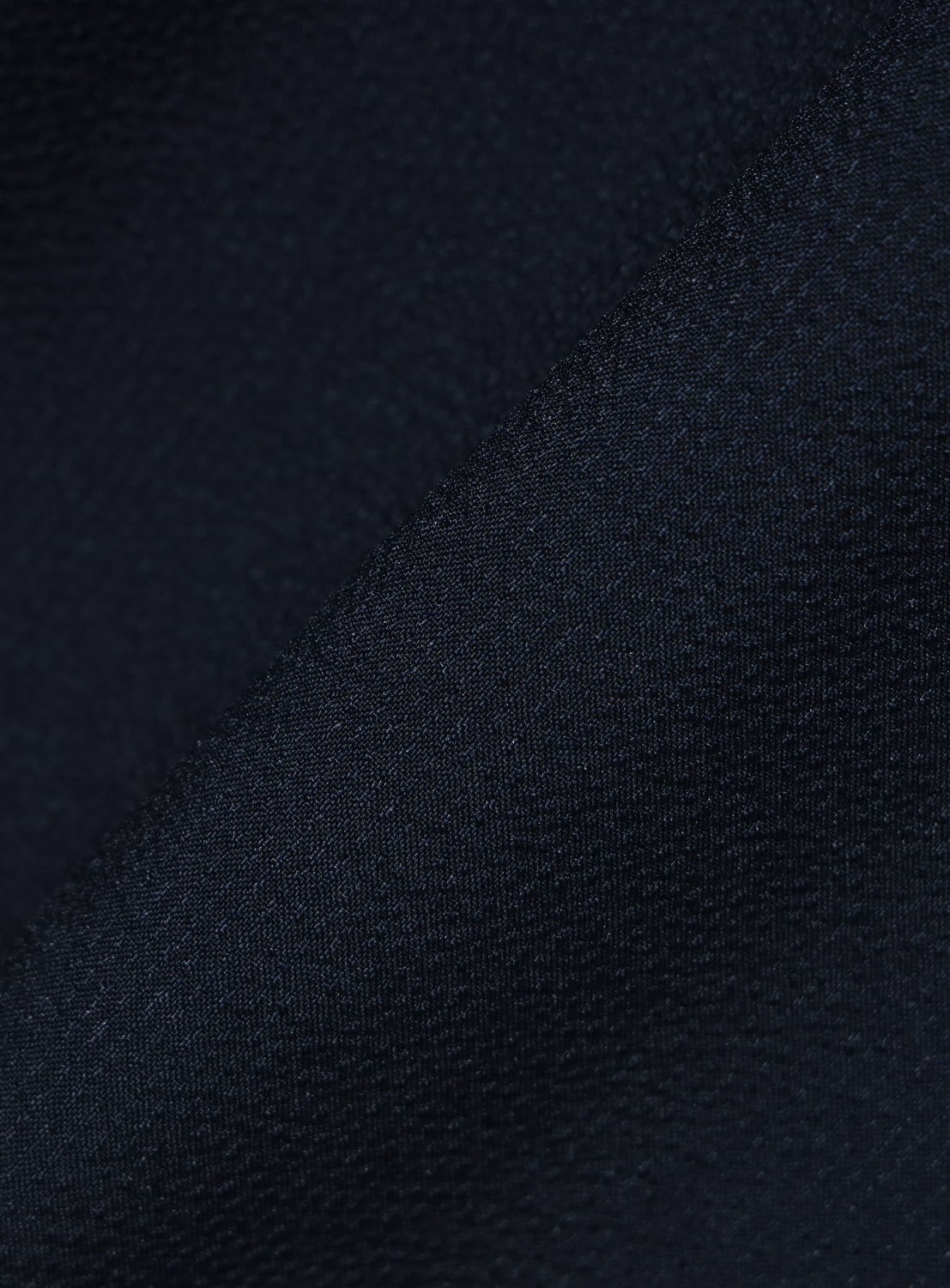 Close-up of dark navy blue fabric with a diagonal fold, highlighting its smooth and subtly textured surface—ideal for the BEAMS Stretch Quick-Dry Seersucker Relaxed Fit Shirt.