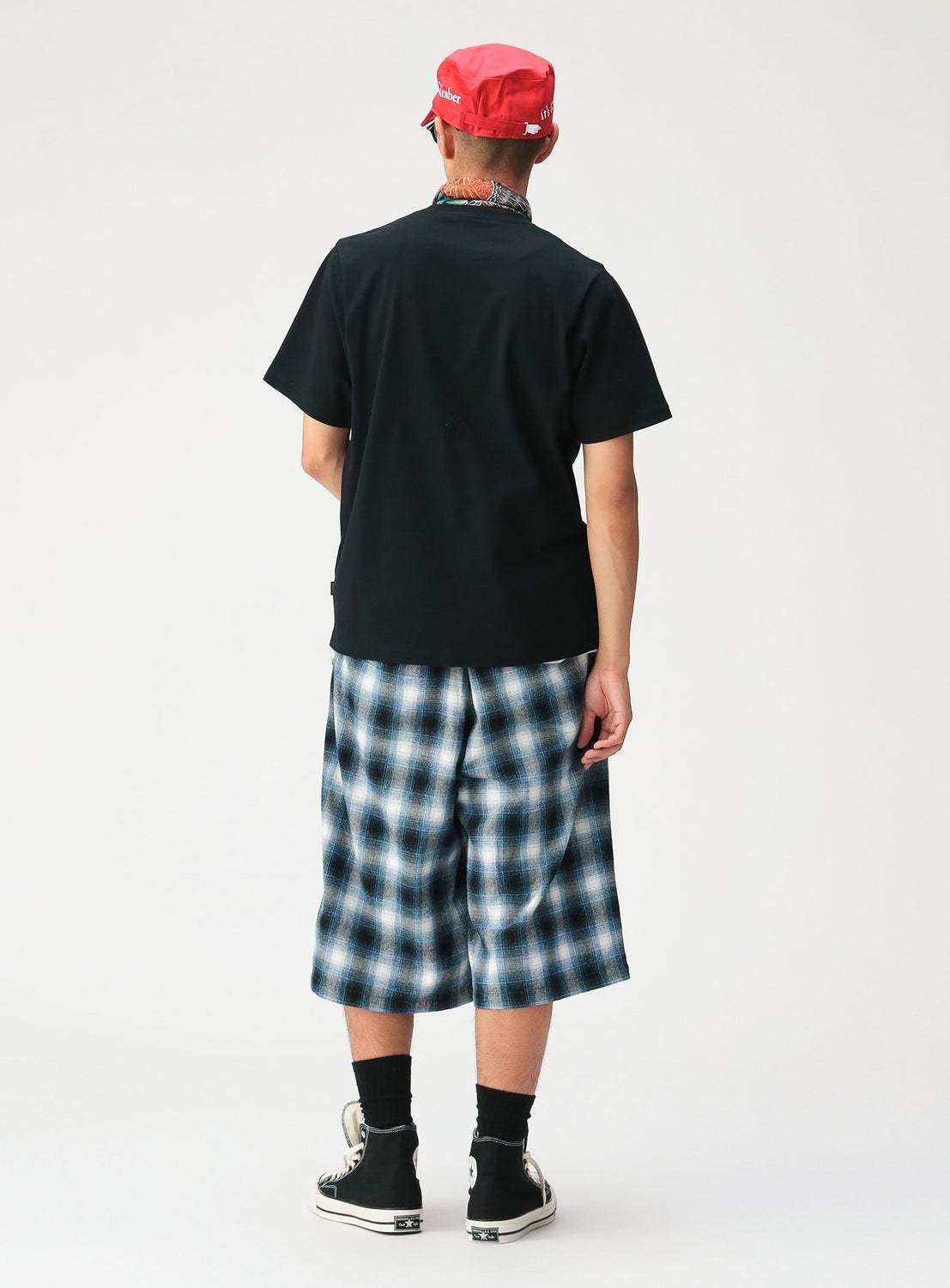 A person seen from behind wearing a black t-shirt, relaxed fit BEAMS Check Shorts, a red cap, and black high-top sneakers.
