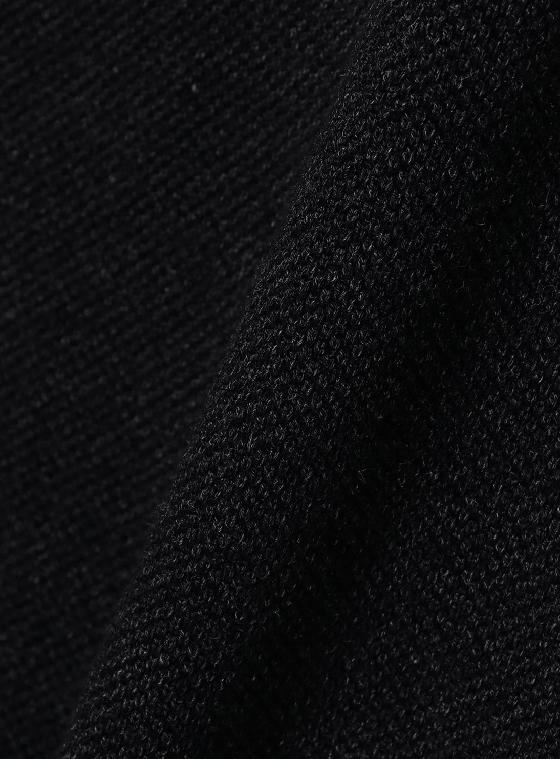 Close-up of crepuscule’s Moss Stitch Skipper Polo Shirt in black, featuring diagonally folded fabric with a visible weave and fibers reminiscent of moss stitch, highlighting the shirt's intricate texture and detail.