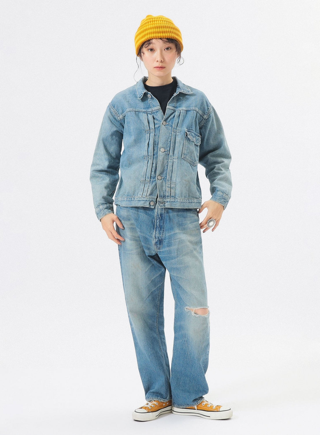 Person wearing a denim jacket and jeans with a yellow beanie on a white background