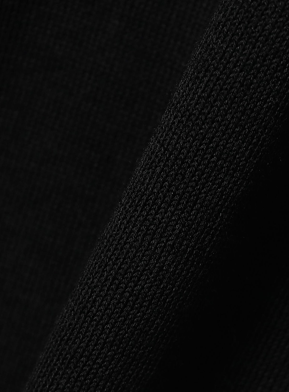 Close-up of crepuscule Short Sleeve Polo in black, showing textured knit fabric with a diagonal fold, fine stitching details, and the soft, polished finish of this premium material.