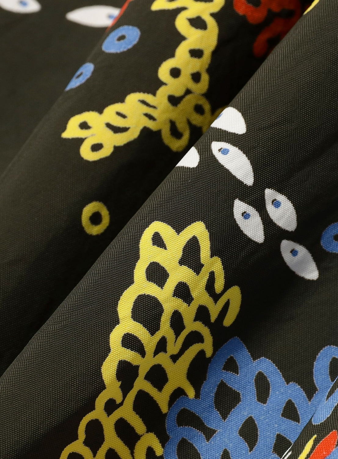 A close-up of black fabric with abstract yellow, red, blue, and white patterns evokes vintage Hawaiian prints in a modern style—perfect for the [Exclusive] SUN SURF x BEAMS BOY Aloha Gathered Long Skirt by SUN SURF.