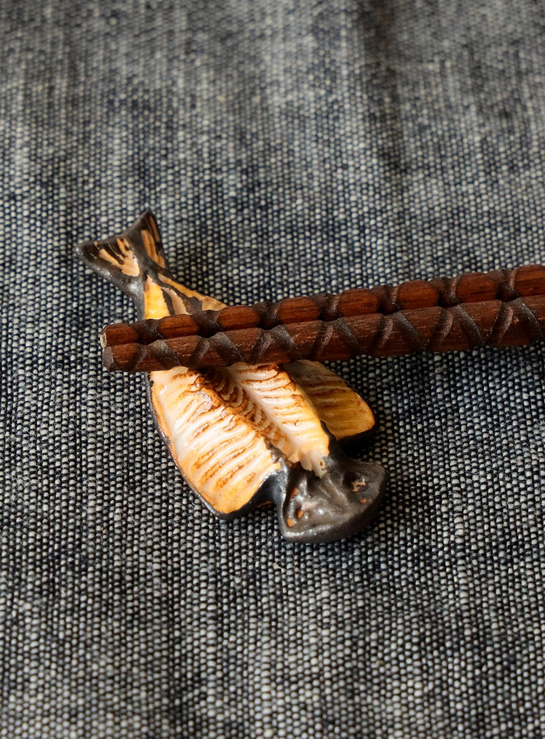 Fish-shaped chopstick rest with wooden chopsticks on a textured background