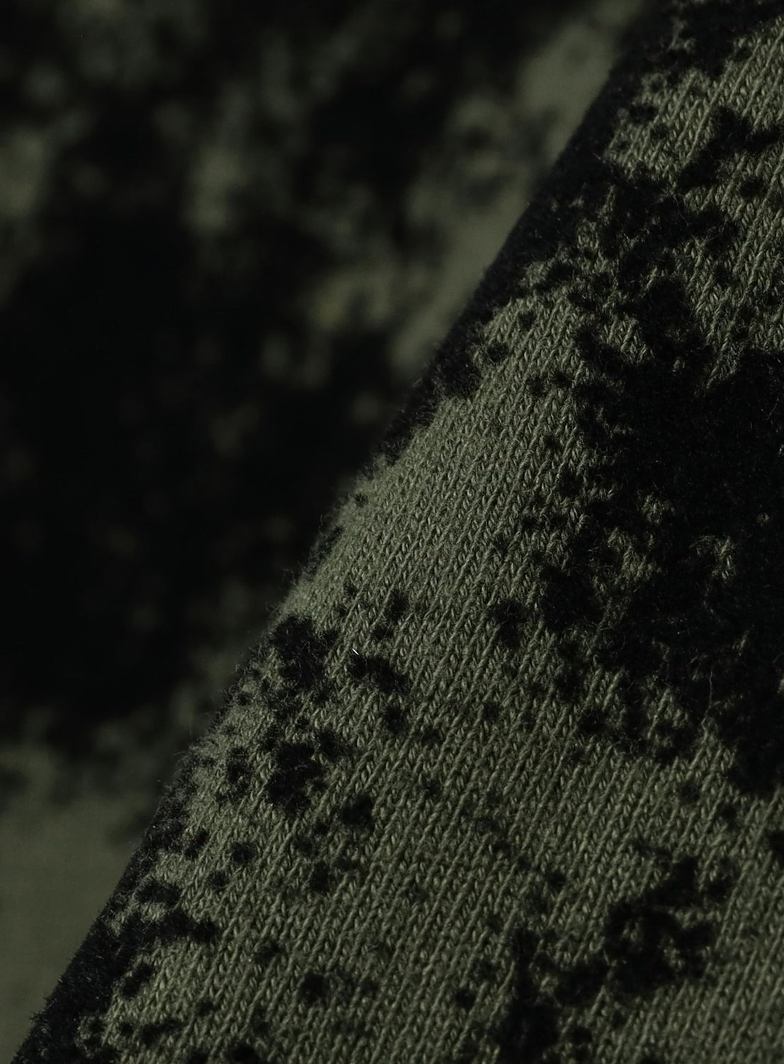 Close-up of a BEAMS Flocked Planet Motif Full-Zip Hoodie, featuring olive green fabric with a black, textured flock print in an abstract planet-like pattern.