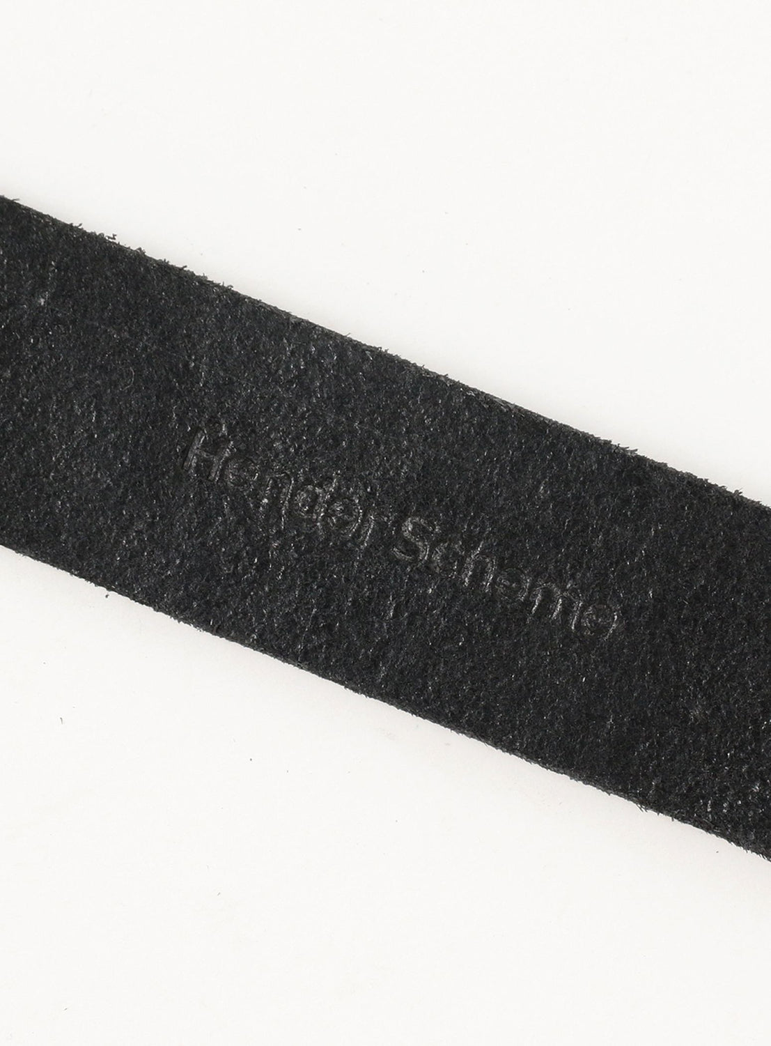 A close-up of the Hender Scheme Tanning Belt, made from premium black cow leather, shows its embossed branding subtly visible against a plain white background.