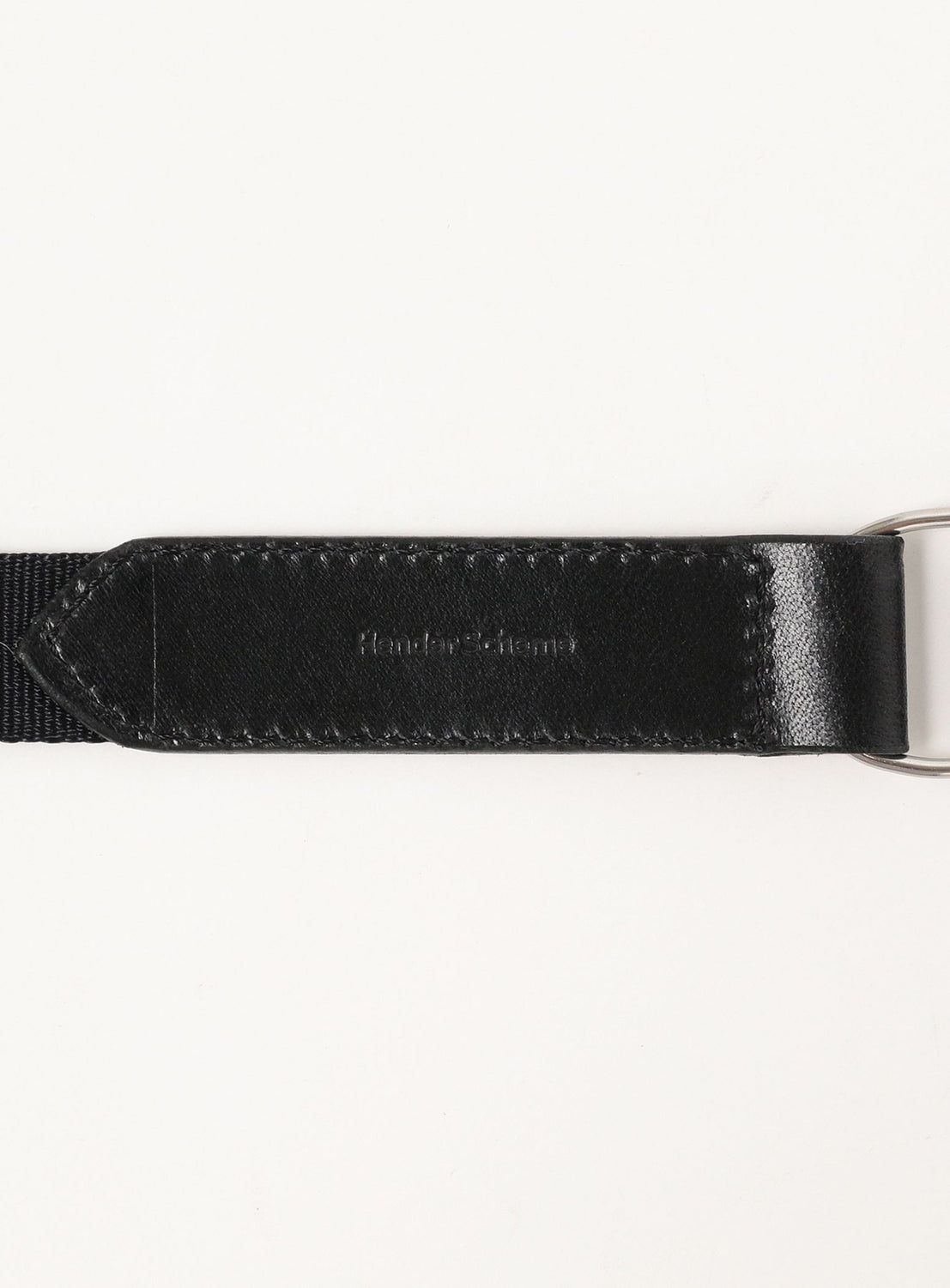 Close-up of the Hender Scheme Fidlock Nylon Belt, showing its black leather and fabric strap with a metal ring on the right, embossed leather text, and FIDLOCK magnetic buckle against a white background.
