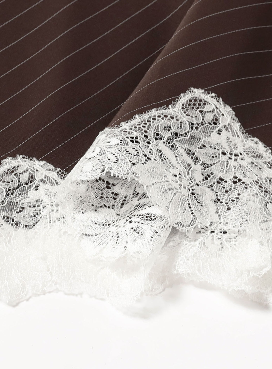 Close-up of the KANAKO SAKAI Lace Trimmed Slip Dress, featuring rich brown regimental stripe fabric accented with a delicate white lace trim along the edge; intricate floral lace details stand out against the smooth, dark material—an exquisite choice for refined elegance.