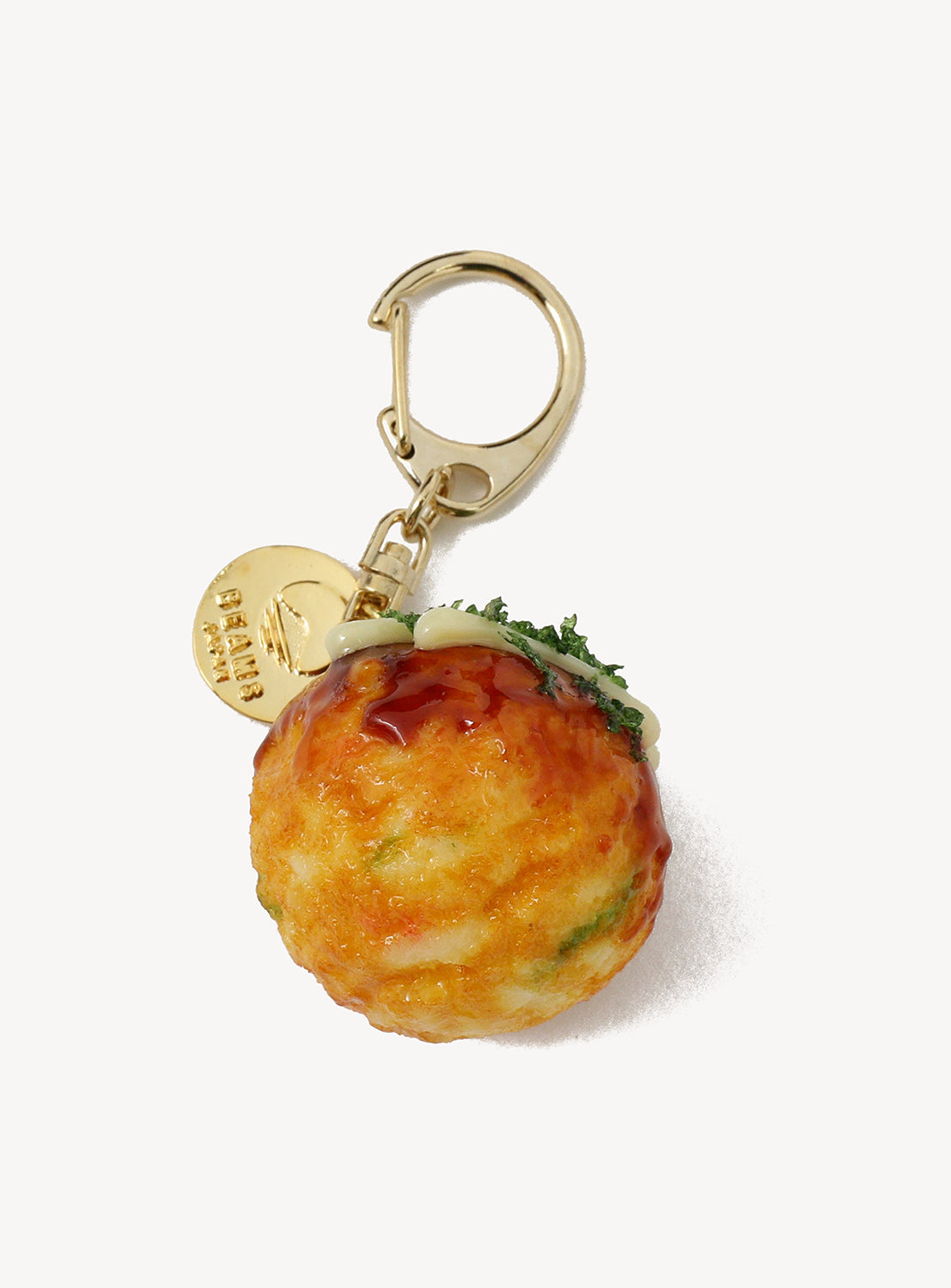 The [Exclusive] BEAMS JAPAN Sample Kobo Realistic Food Sample Keychain - Vol. 1 by BEAMS JAPAN features a lifelike takoyaki charm, complete with sauce, mayonnaise, and green garnish details. This charming handmade keychain is attached to a gold-colored clasp and round tag—an authentic Japan souvenir inspired by Gujo Hachiman’s iconic food sample keychains.