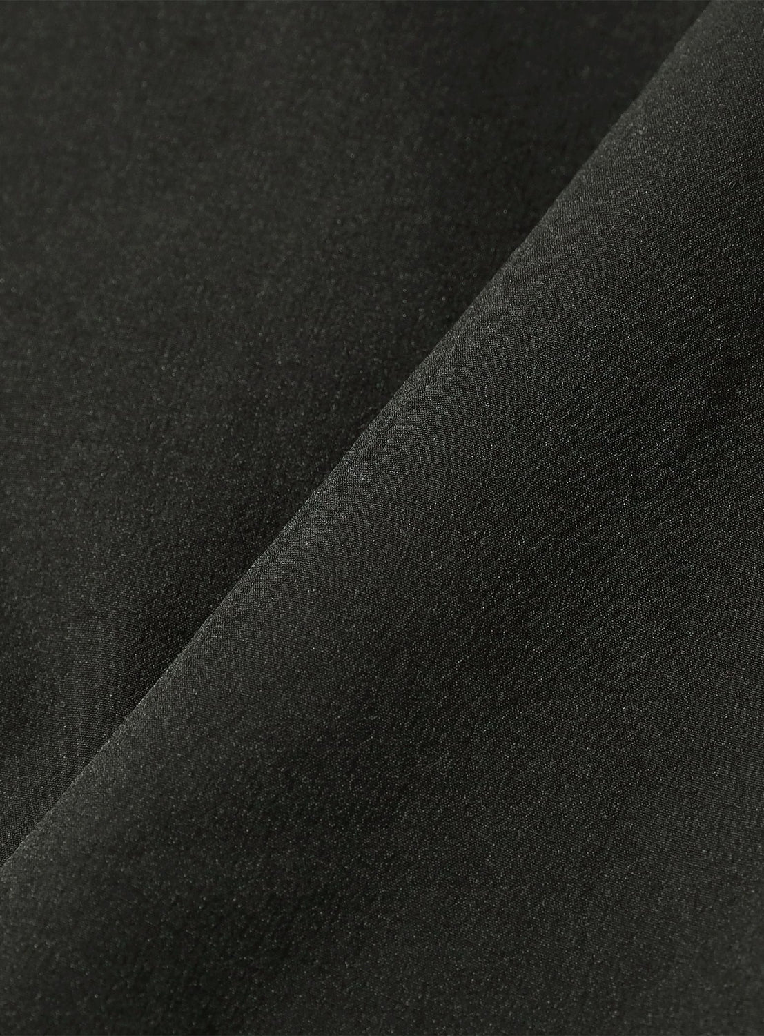 A close-up of a folded piece of smooth, black stretch fabric from the BEAMS Tech Shirt.