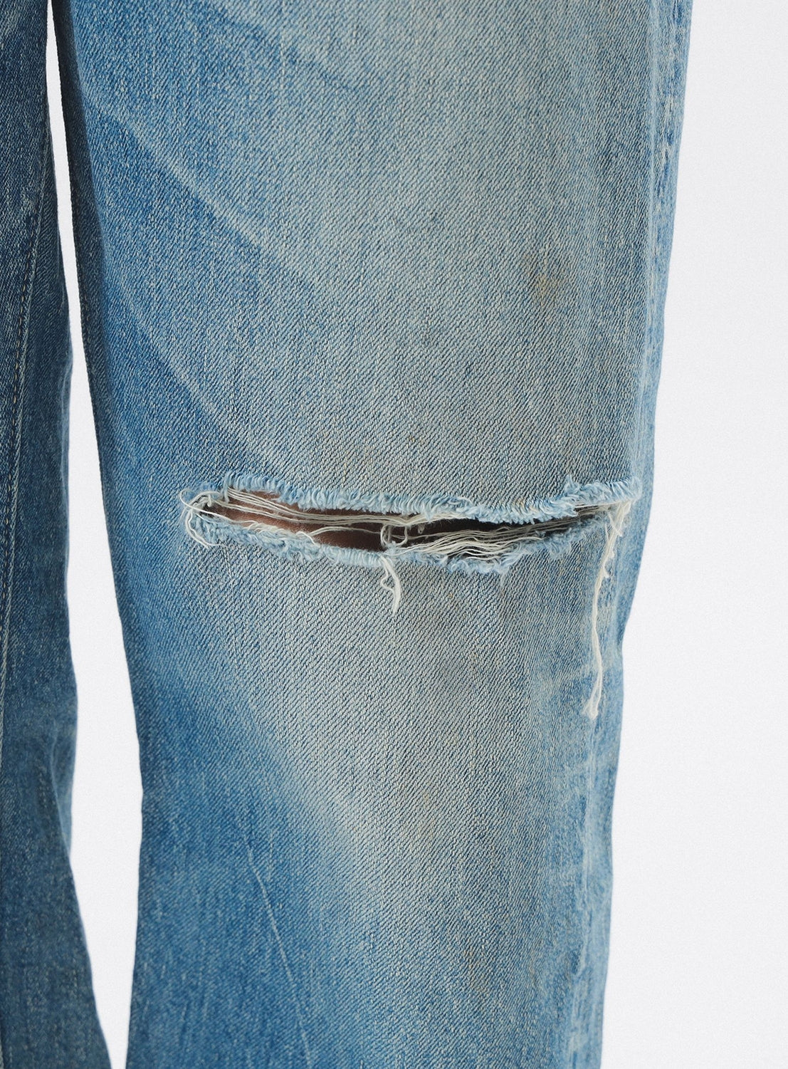 Close-up of a blue denim jeans with a ripped knee on a white background