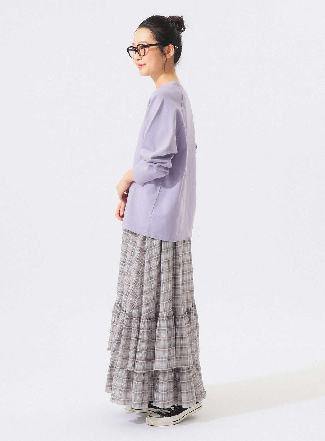 A woman wearing glasses, a light purple long-sleeved top, the BEAMS BOY Check Tiered Skirt crafted from lightweight fabric, and black sneakers stands in profile against a plain white background.
